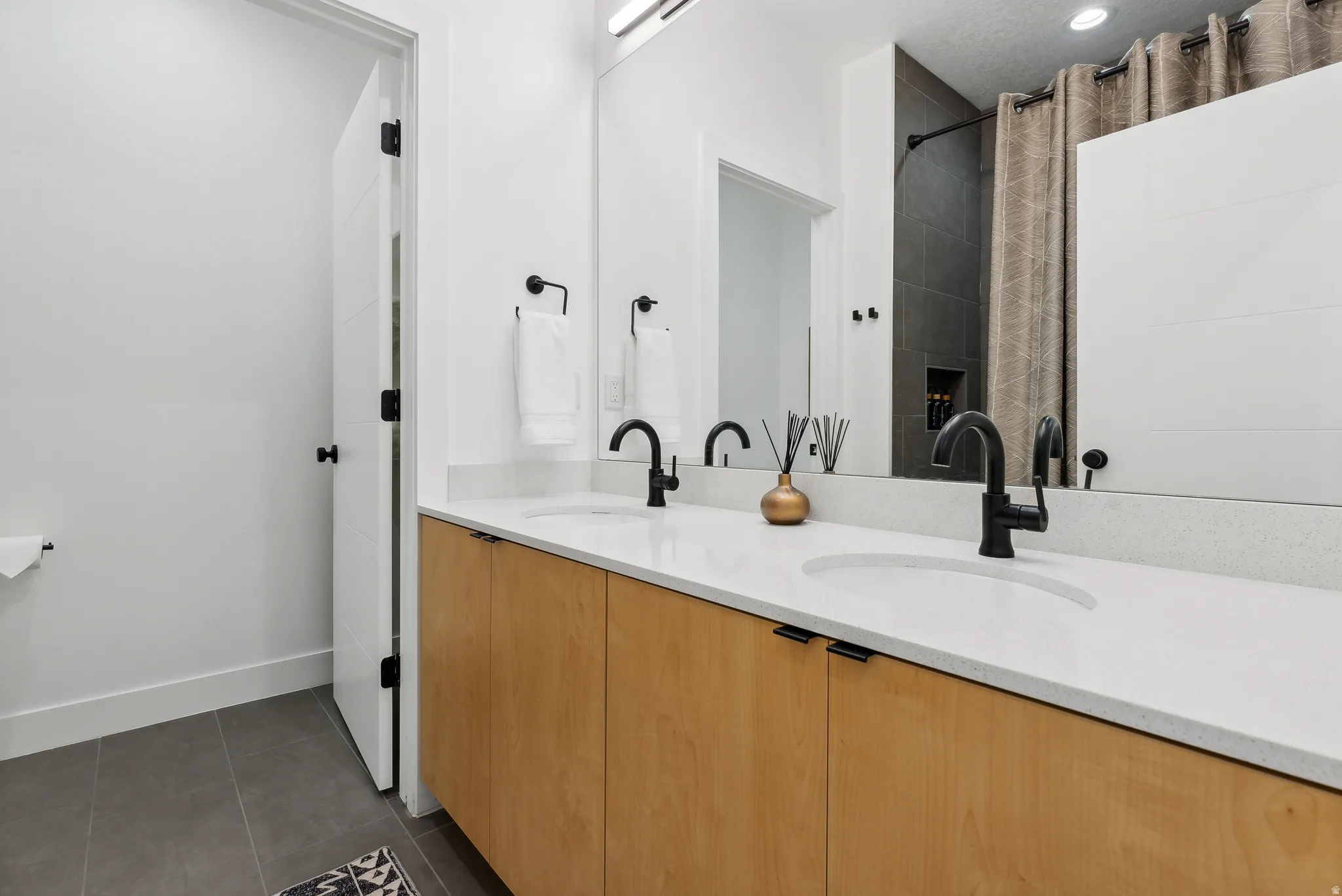 Bathroom vanity featuring a light wood-finish double cabinet, white countertop with integrated sinks, and matte black fixtures