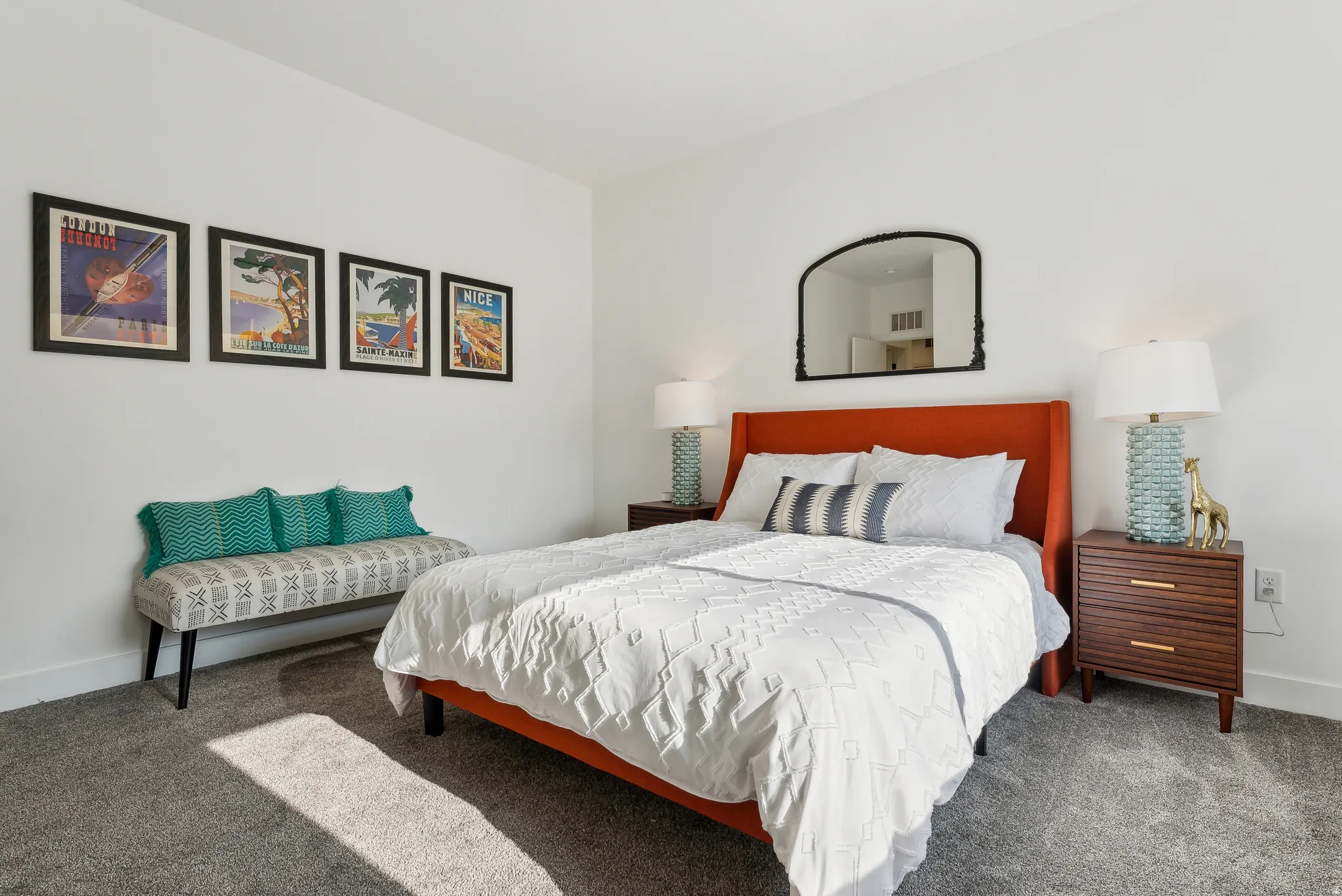 Carpeted room featuring white walls, a built-in wall mirror, and a patterned upholstered bench