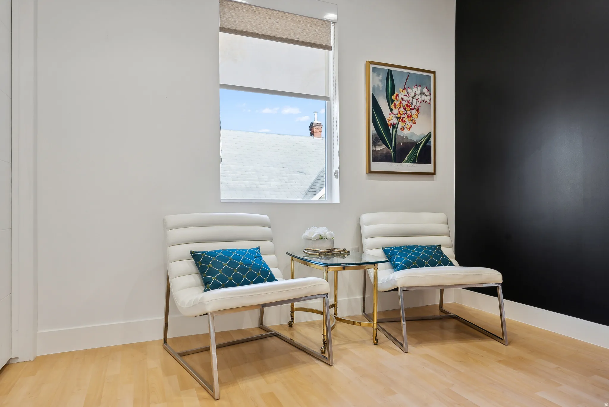 Bright room featuring a window with a roller shade, wood-finish flooring, white walls, and a contrasting dark accent wall