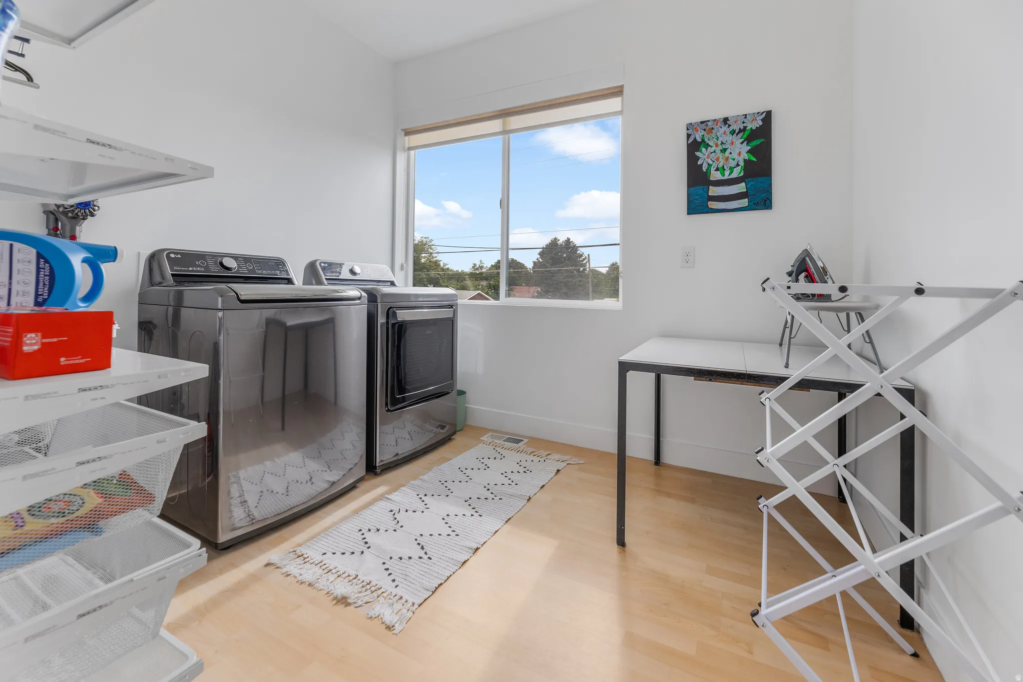 Bright utility room featuring light wood-finish flooring, a large window, and white walls