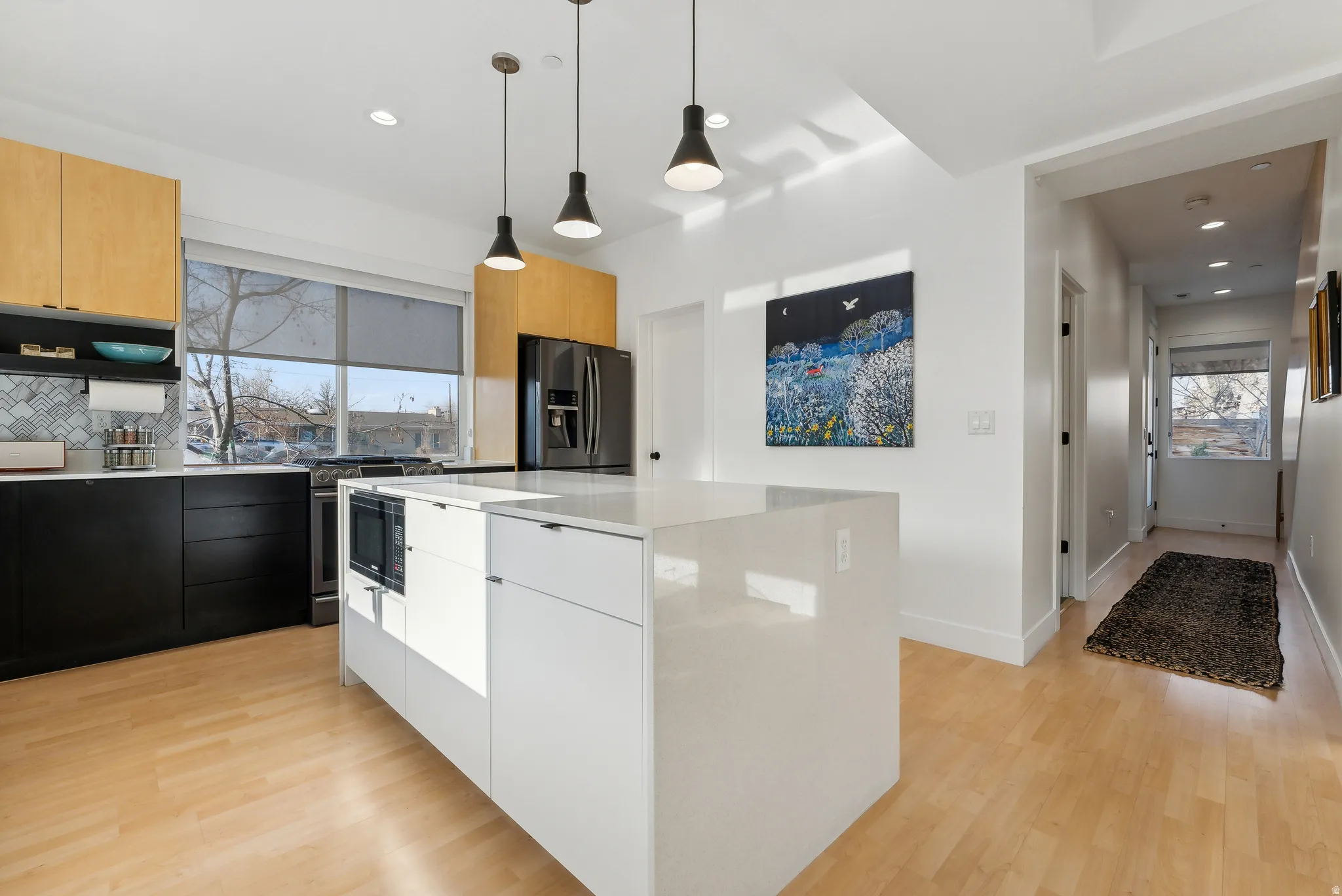 Kitchen featuring a large central island with a built-in microwave, light wood-finish flooring, and a patterned tile backsplash
