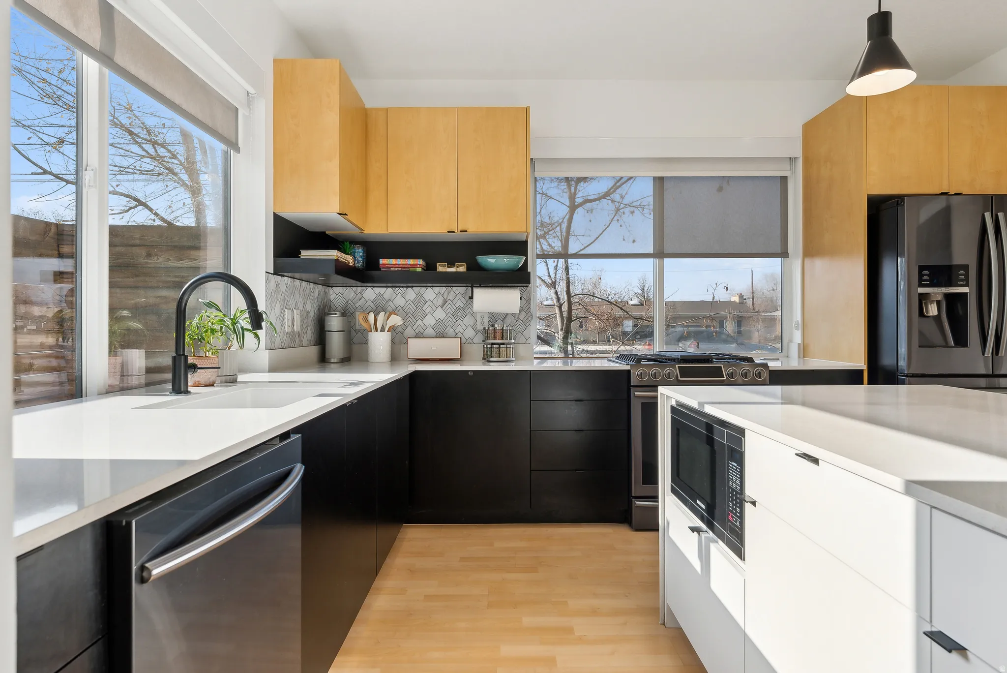 Modern kitchen featuring light wood-finish upper cabinetry, black lower cabinetry, and a white center island