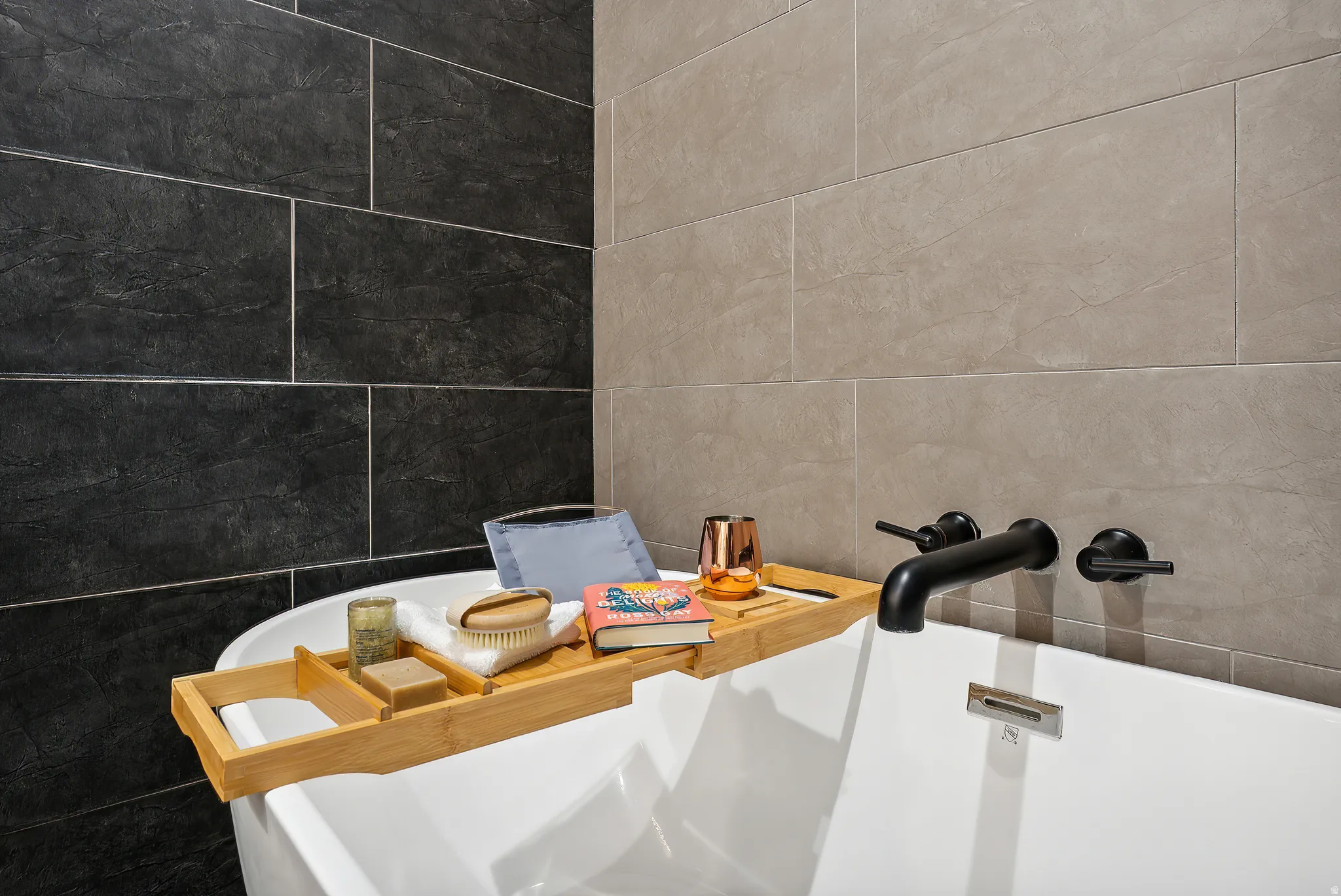 Freestanding white soaking tub with matte black wall-mounted faucet and controls
