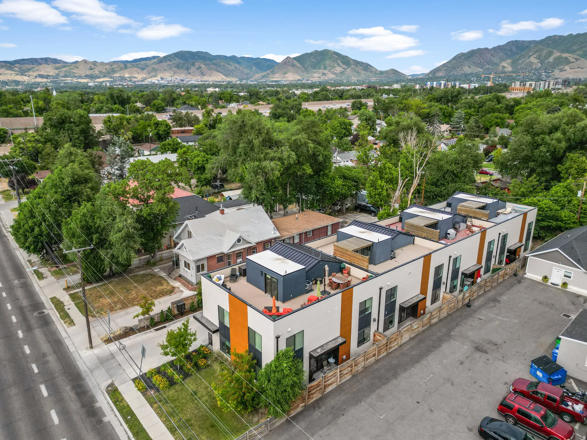 Modern multi-story residential complex featuring white and wood-tone facades, individual rooftop patios, and private ground-level outdoor spaces