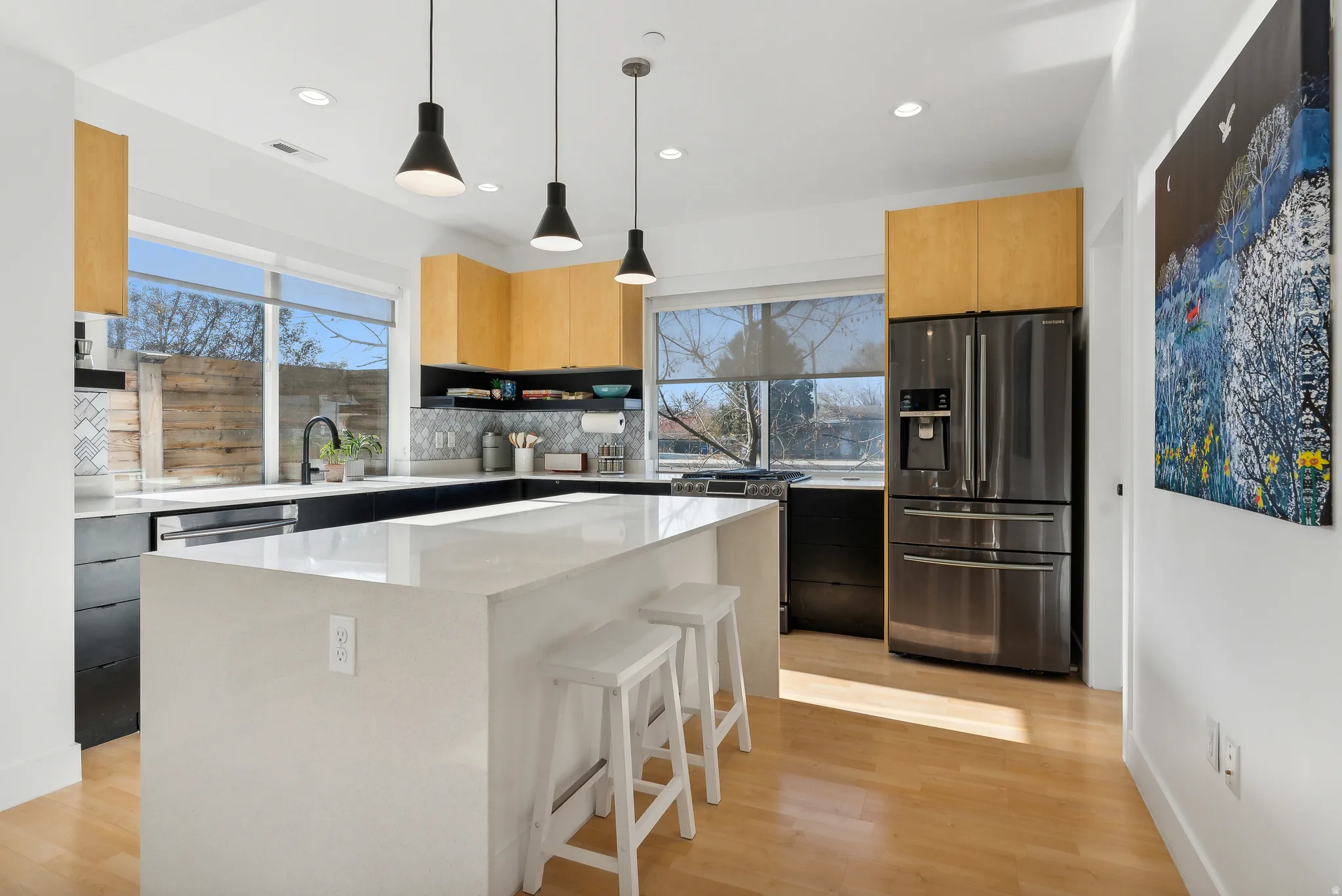 Modern kitchen featuring a large center island with a light-toned countertop, wood-finish flooring, two-tone cabinetry, and sleek pendant lighting