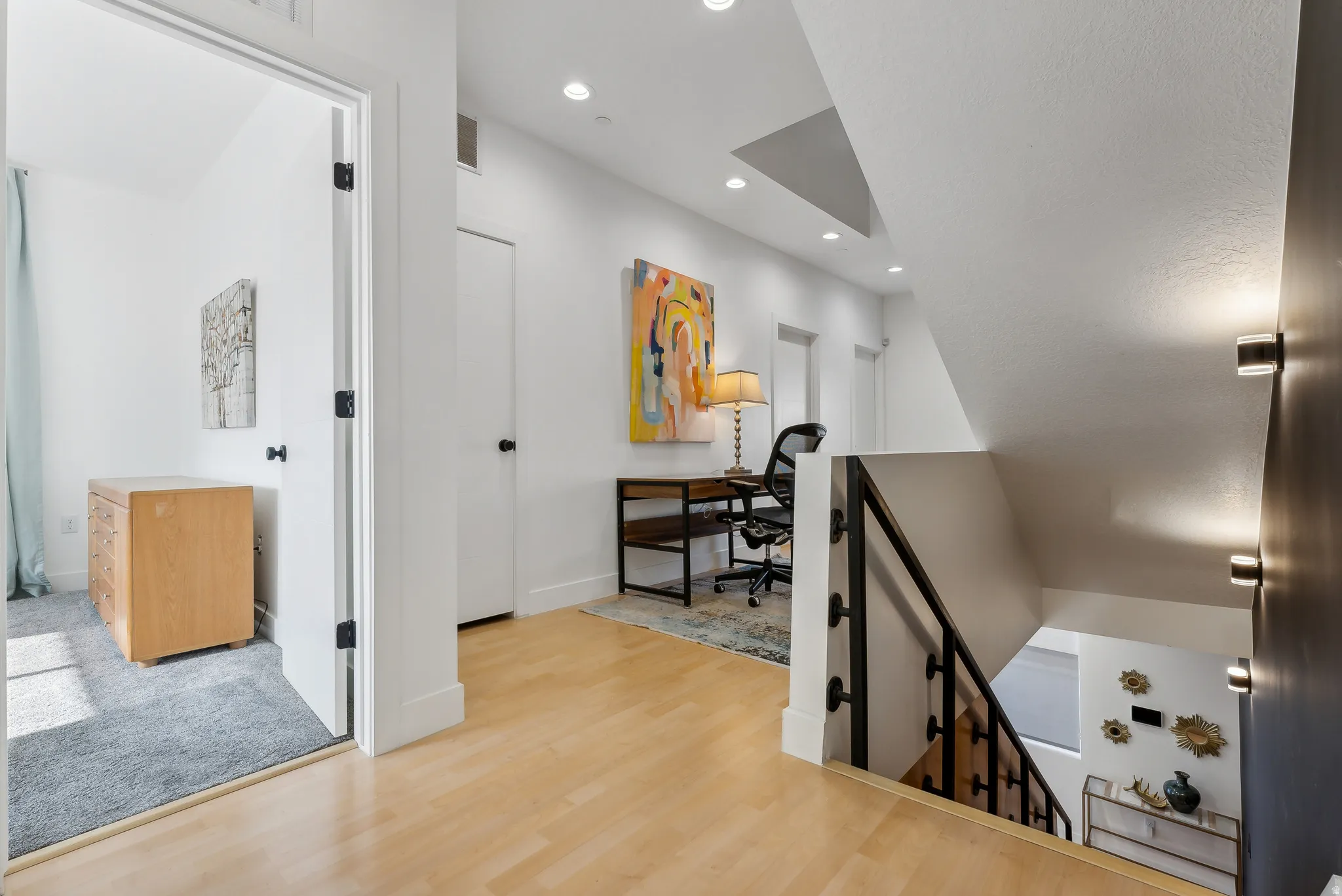Wood-finish flooring defines this upper-level landing, featuring recessed lighting and a contemporary black metal stair railing
