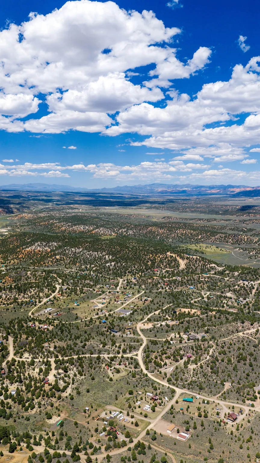 Expansive aerial landscape featuring a rural development with scattered residences, natural green foliage, and winding unpaved roads