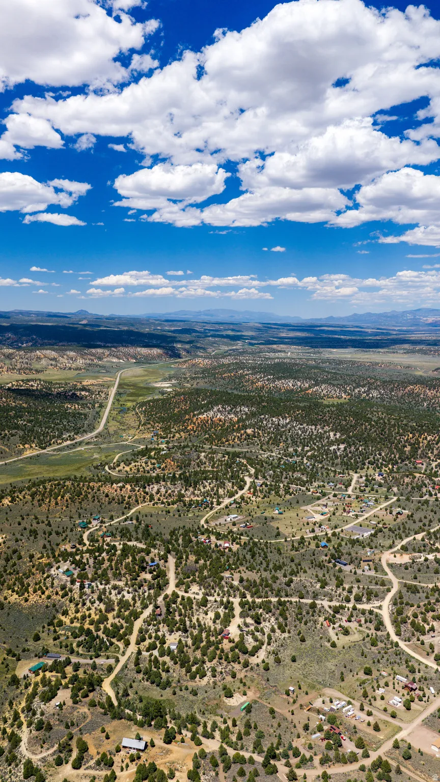 Expansive aerial landscape featuring scattered residential properties, winding unpaved roads, and dense natural foliage