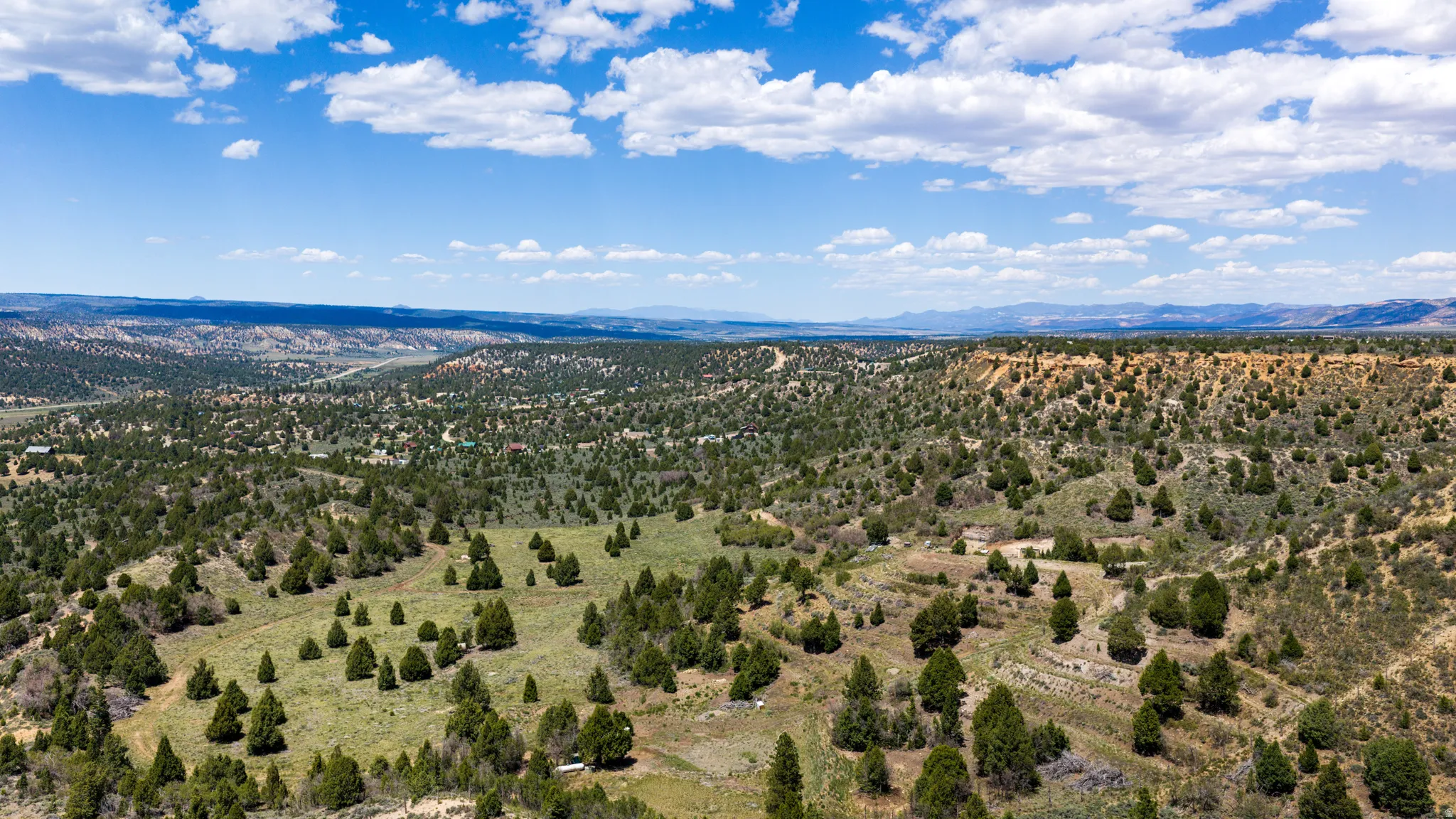 Expansive landscape featuring rolling hills, varied terrain, scattered evergreen trees, and distant mountain ranges