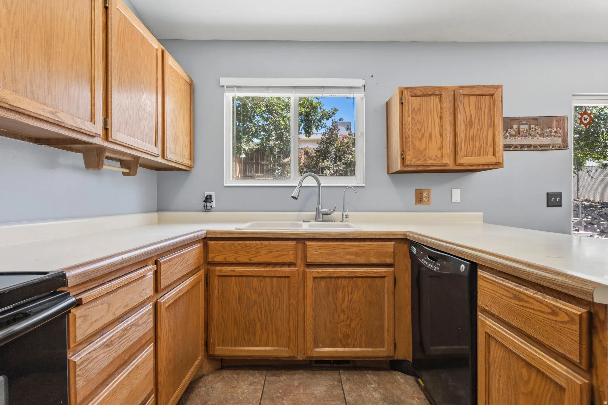 Kitchen featuring wood cabinetry, light-toned countertops, a dual-basin sink with a gooseneck faucet, and a built-in dishwasher