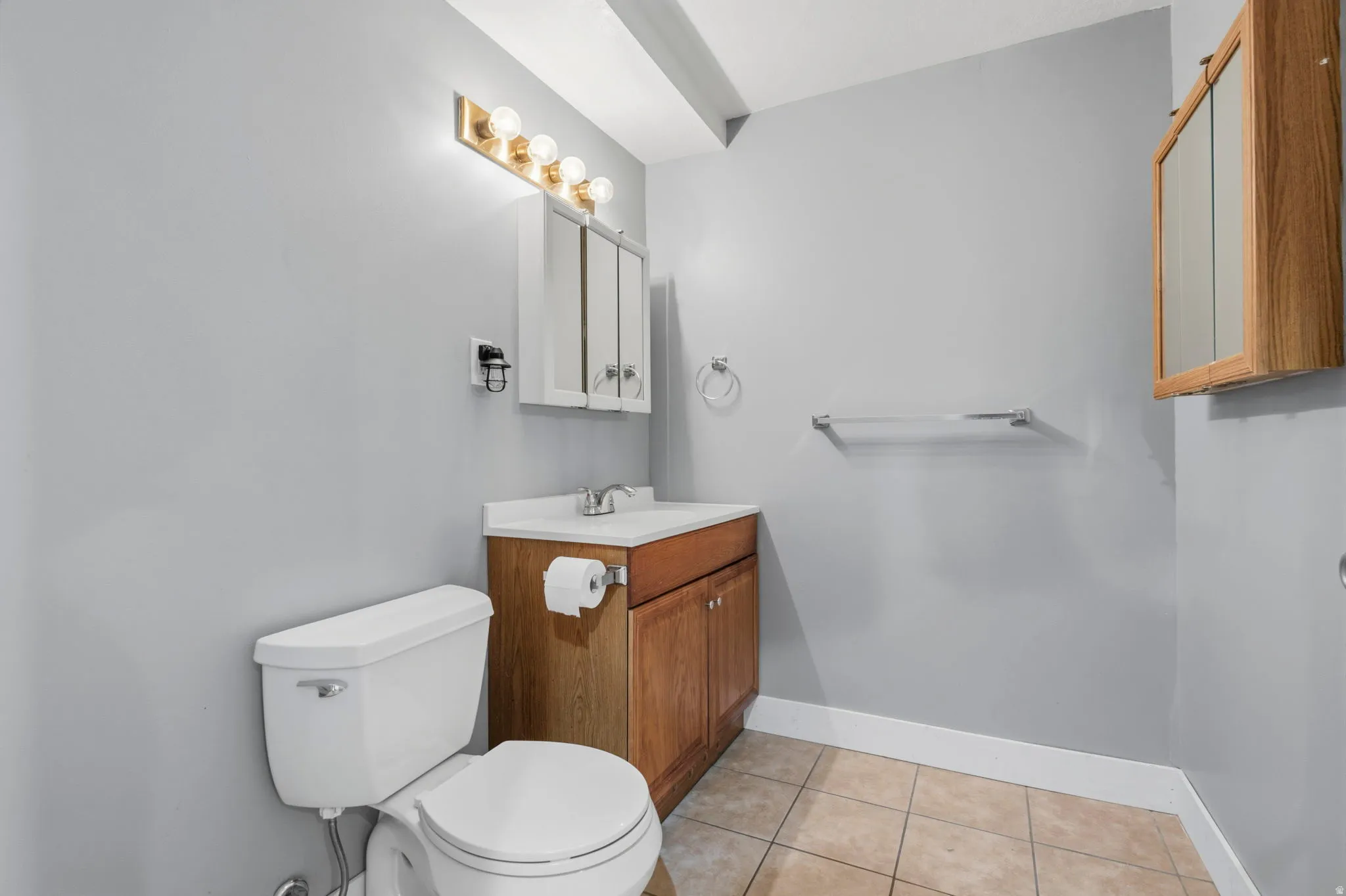 Neutral tone bathroom featuring a porcelain toilet, wood-finish vanity with countertop sink, and a mirrored medicine cabinet