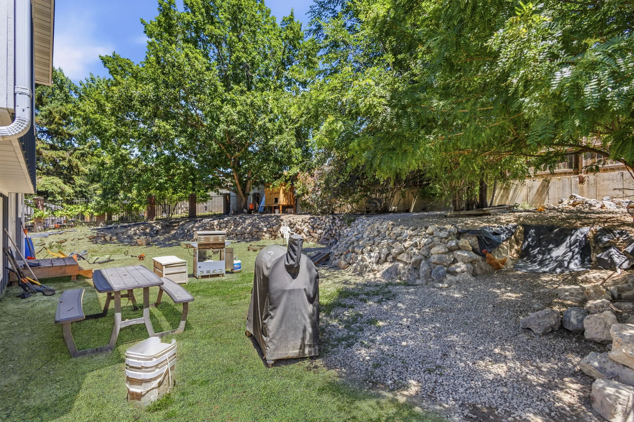 Expansive backyard featuring mature trees, a manicured lawn, and a multi-level terraced landscape with natural rock retaining walls