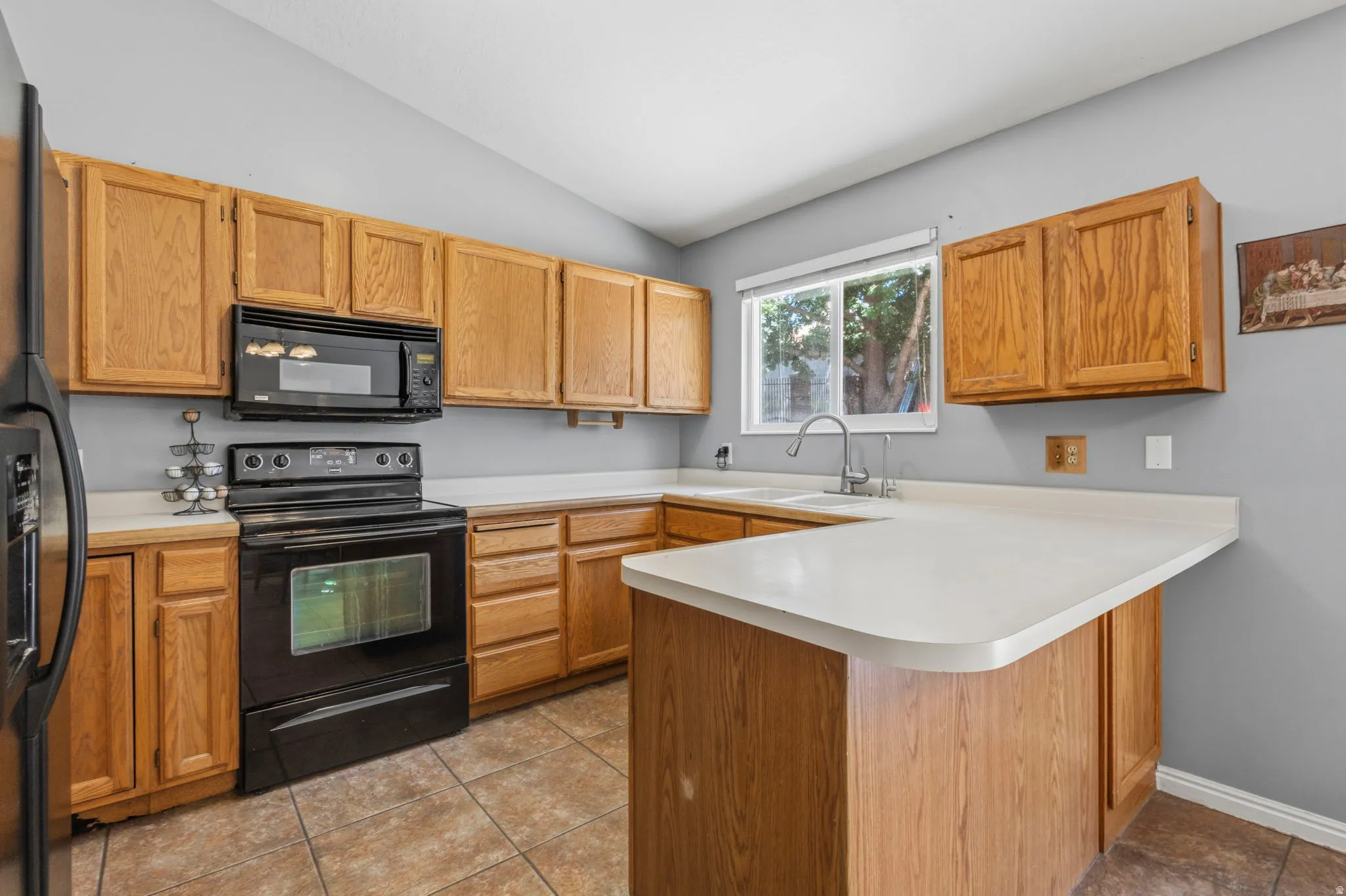 Kitchen featuring wood cabinetry, light-toned countertops, a black electric range, a built-in microwave, and tile flooring