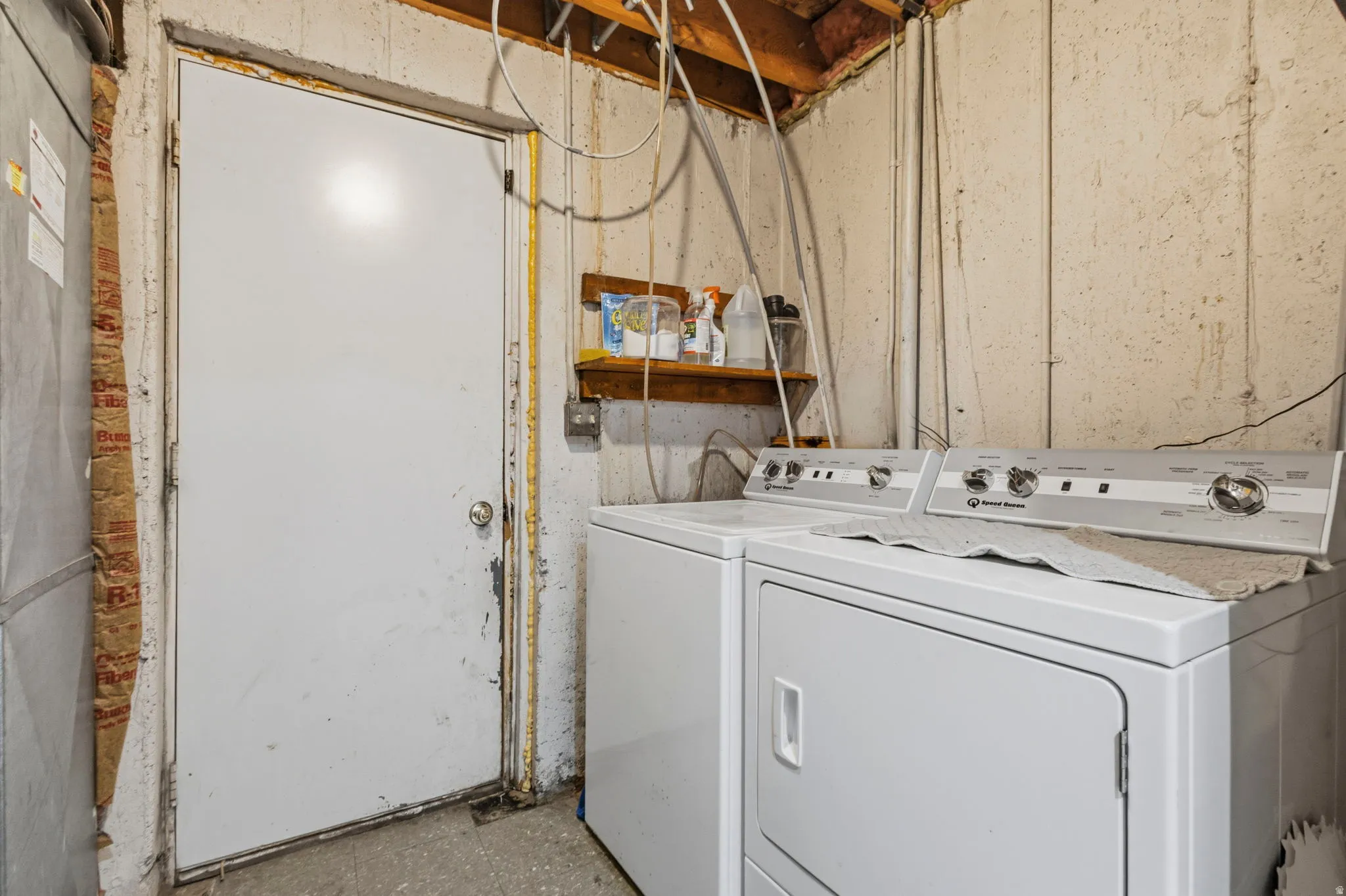 Laundry area featuring concrete block walls and exposed ceiling joists
