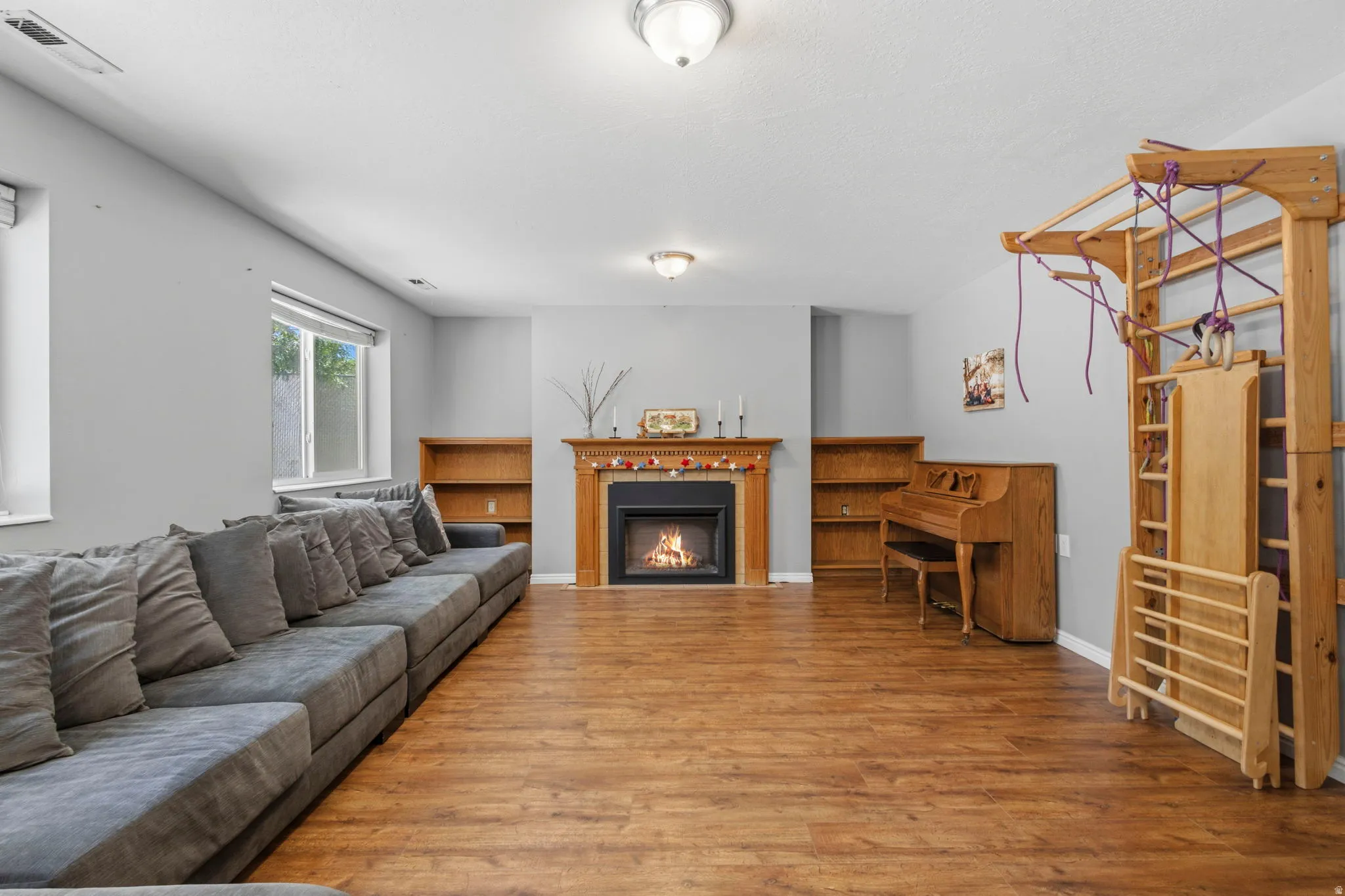 Spacious room with wood-finish flooring, a fireplace with a wood mantel, and built-in shelving
