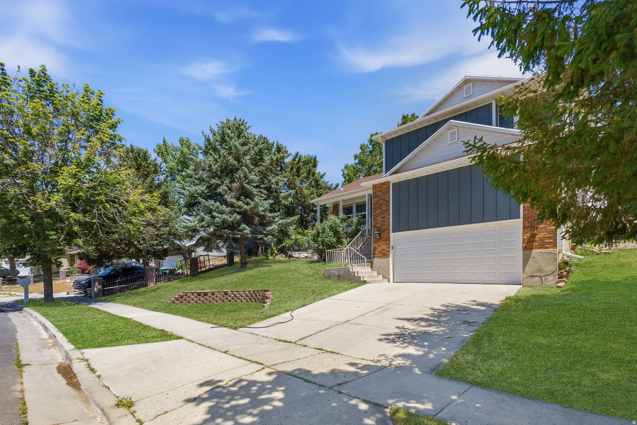 Split-level residence featuring brick and siding exterior, an attached garage, mature landscaping, and a concrete driveway