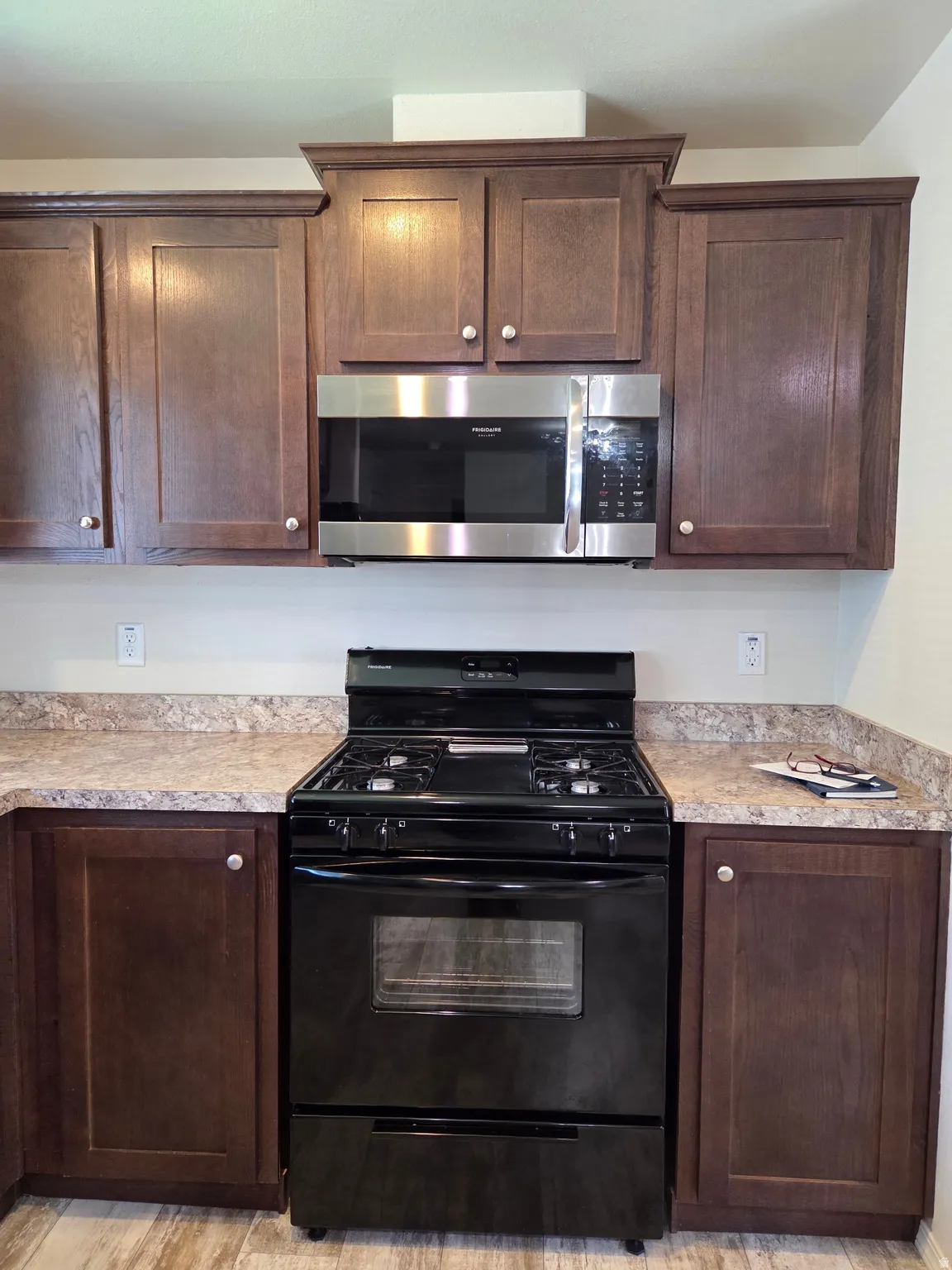 Kitchen featuring a black gas range, a stainless steel over-the-range microwave, and dark wood cabinetry with light-toned countertops