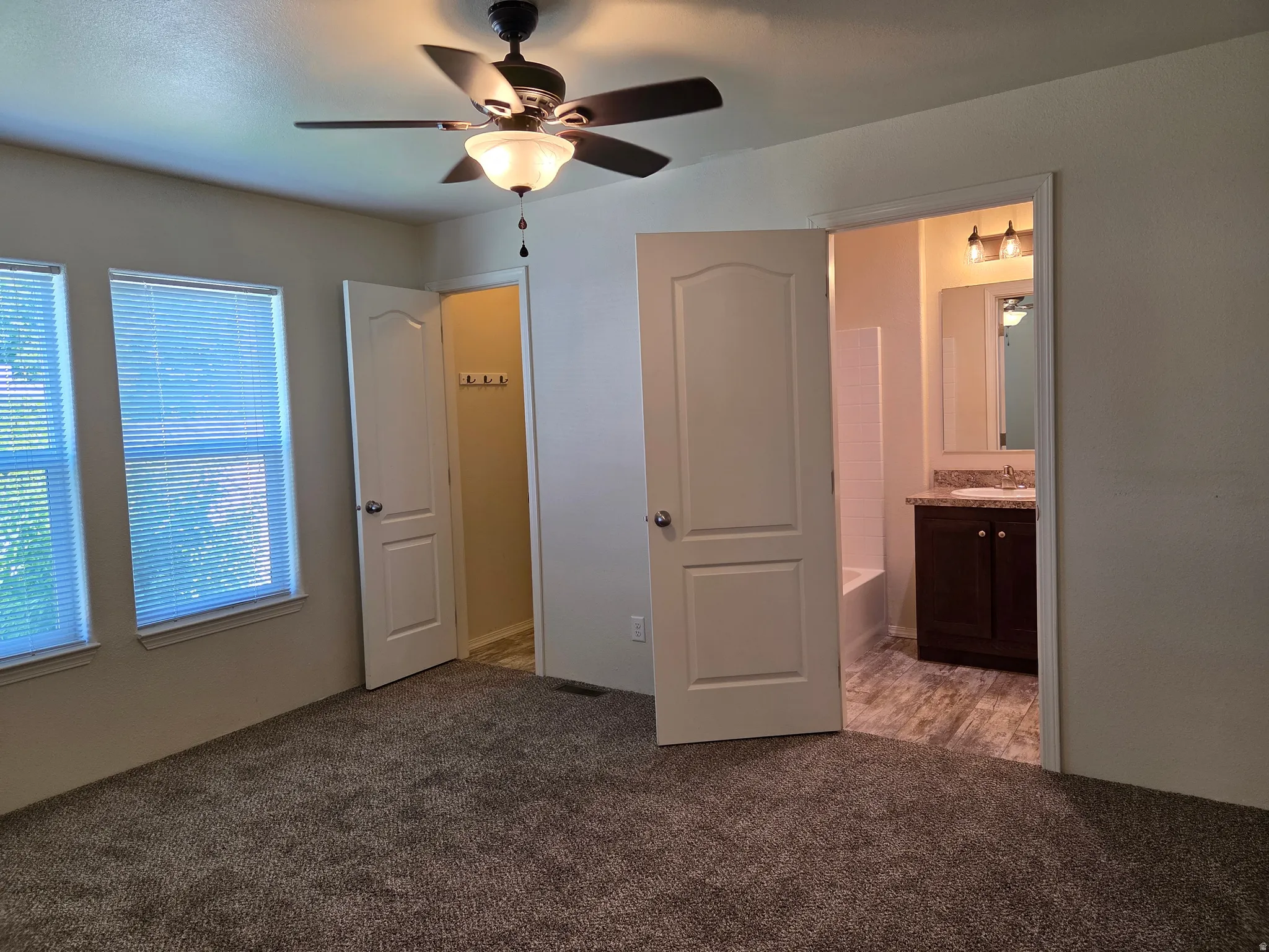 Bedroom featuring carpeting, dual windows, a ceiling fan, and direct access to a full bathroom