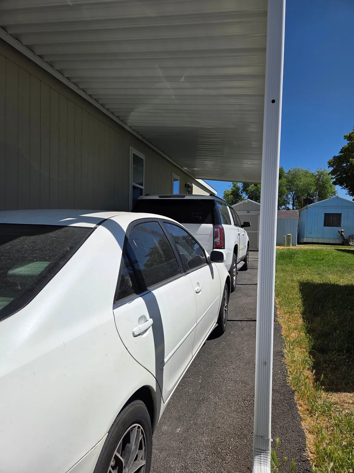 Carport with a corrugated metal roof providing covered parking, paved driveway, light-colored siding