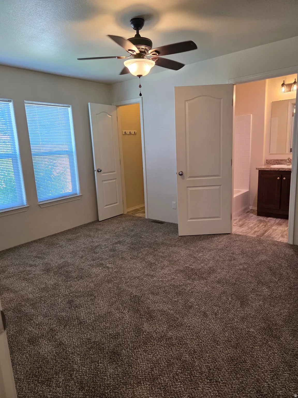 Spacious room featuring neutral carpet flooring, two windows, and a ceiling fan