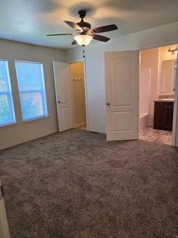 Spacious room featuring neutral carpet flooring, two windows, and a ceiling fan