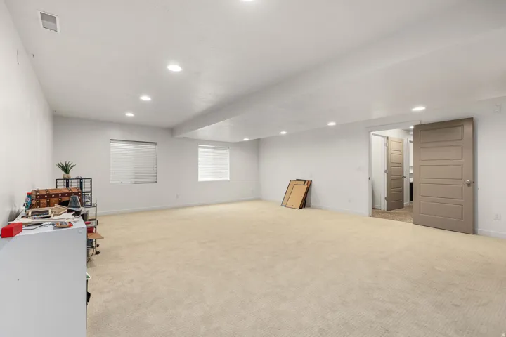 Spacious carpeted room featuring recessed lighting, two windows with horizontal blinds, and a five-panel interior door