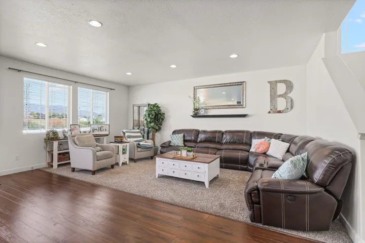 Spacious living area featuring recessed lighting, a large window array, and wood-finish flooring transitioning to an area rug