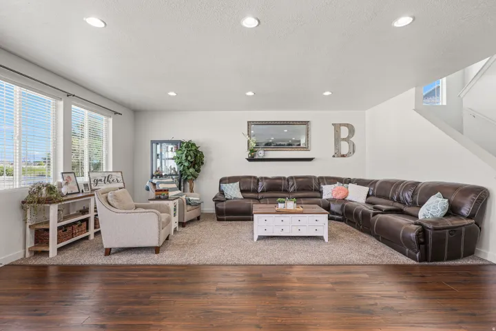 Open living area featuring wood-finish flooring transitioning to carpet, recessed lighting, and a prominent window array with blinds