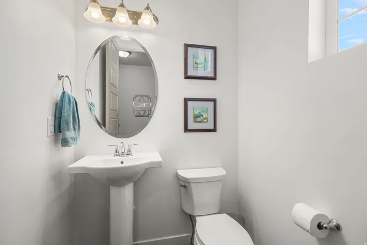 Pedestal sink with chrome faucet, oval mirror, and three-light vanity fixture