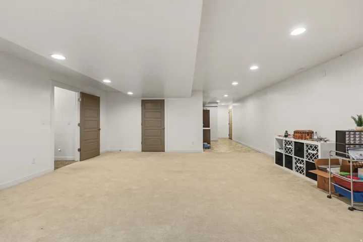Expansive carpeted area with recessed lighting, white walls, and multiple panel doors