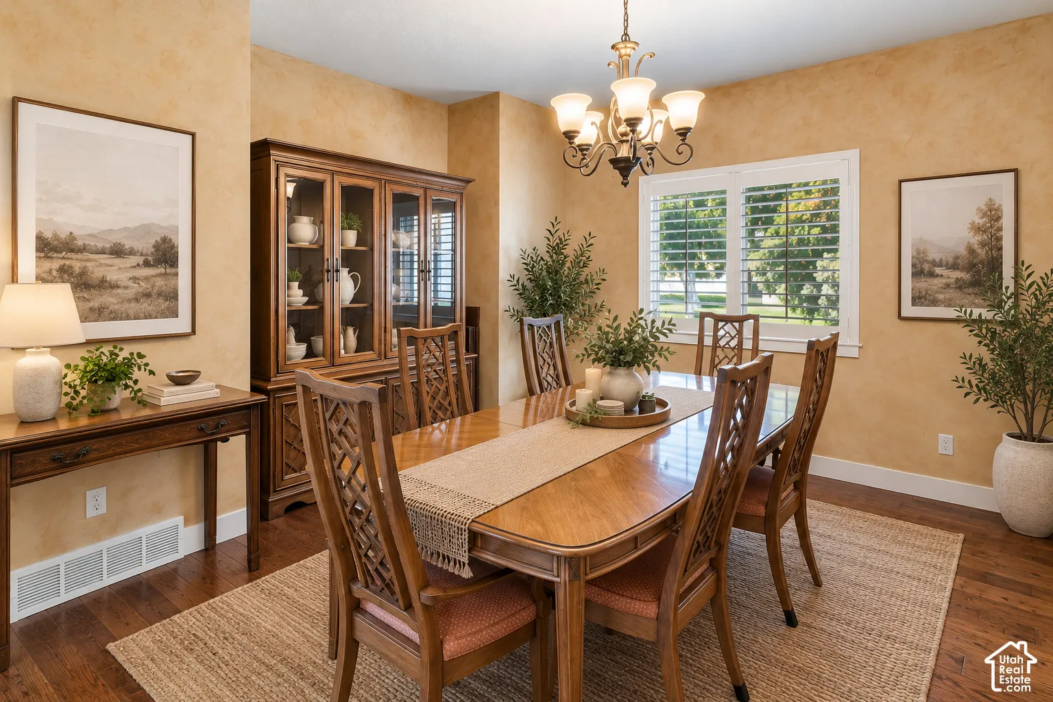 Dining area featuring warm-toned wall finishes, wood-finish flooring, a multi-arm iron chandelier, and white plantation shutters
