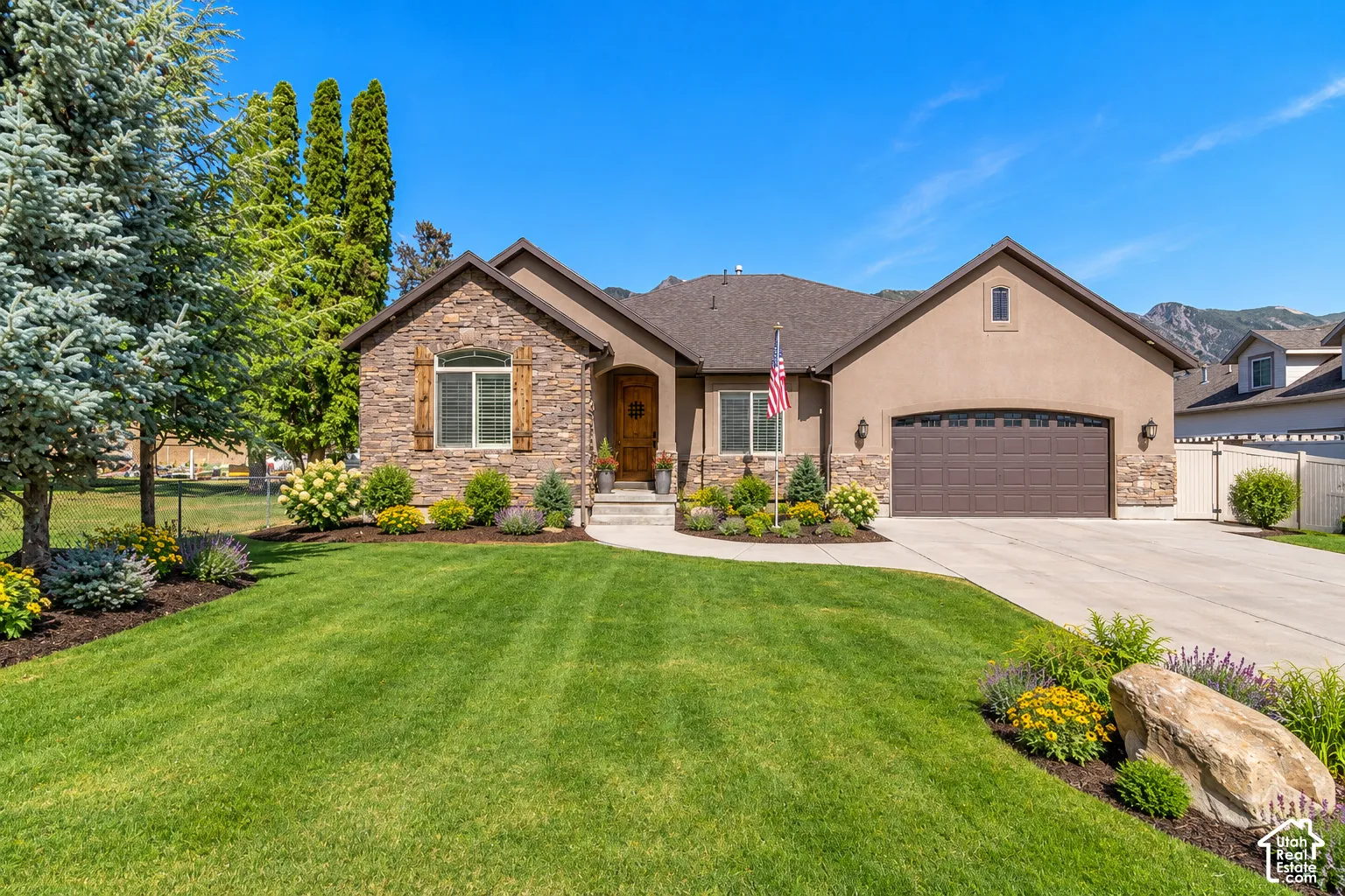 Exterior featuring stone masonry facade, stucco siding, an arched entryway, attached multi-car garage, and landscape elements including manicured lawn and mature plantings