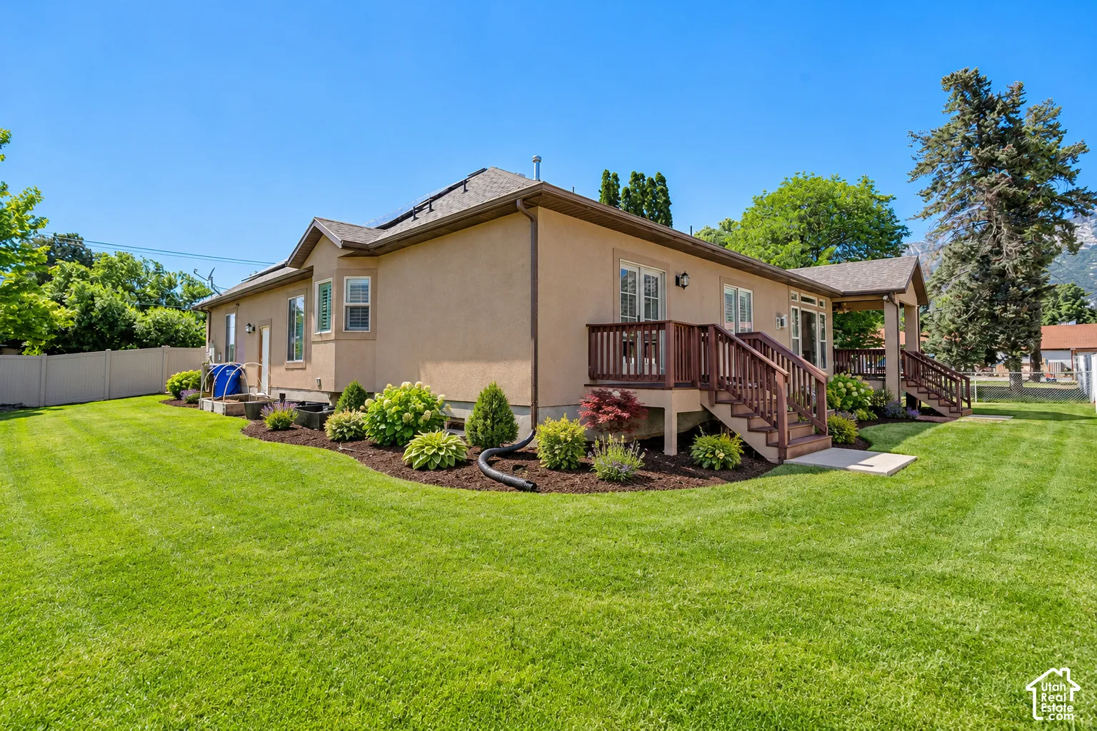 Stucco exterior featuring dual raised wooden decks, mulch-lined landscaping, vinyl fencing, and a manicured lawn