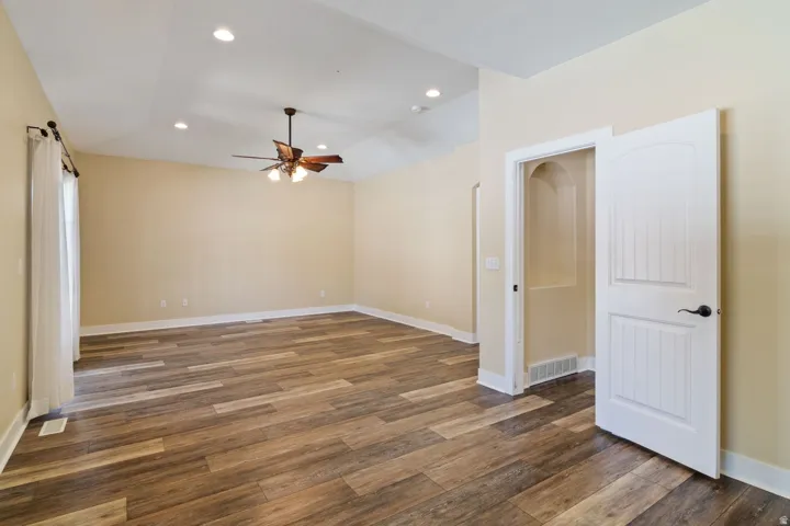 Spacious interior room featuring wood-finish flooring, vaulted ceiling with recessed lighting, and a ceiling fan