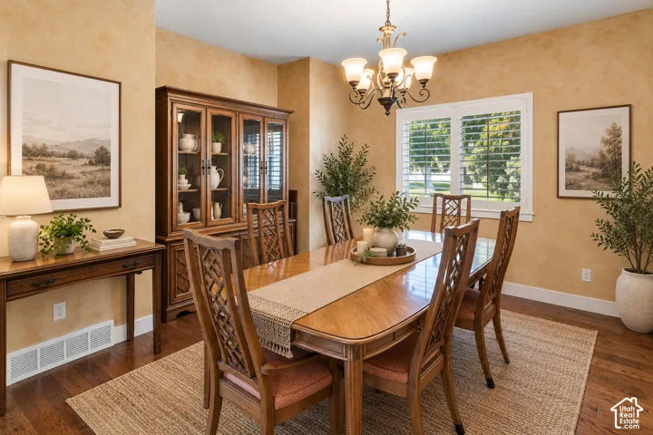 Dining area featuring warm-toned wall finishes, wood-finish flooring, a multi-arm iron chandelier, and white plantation shutters