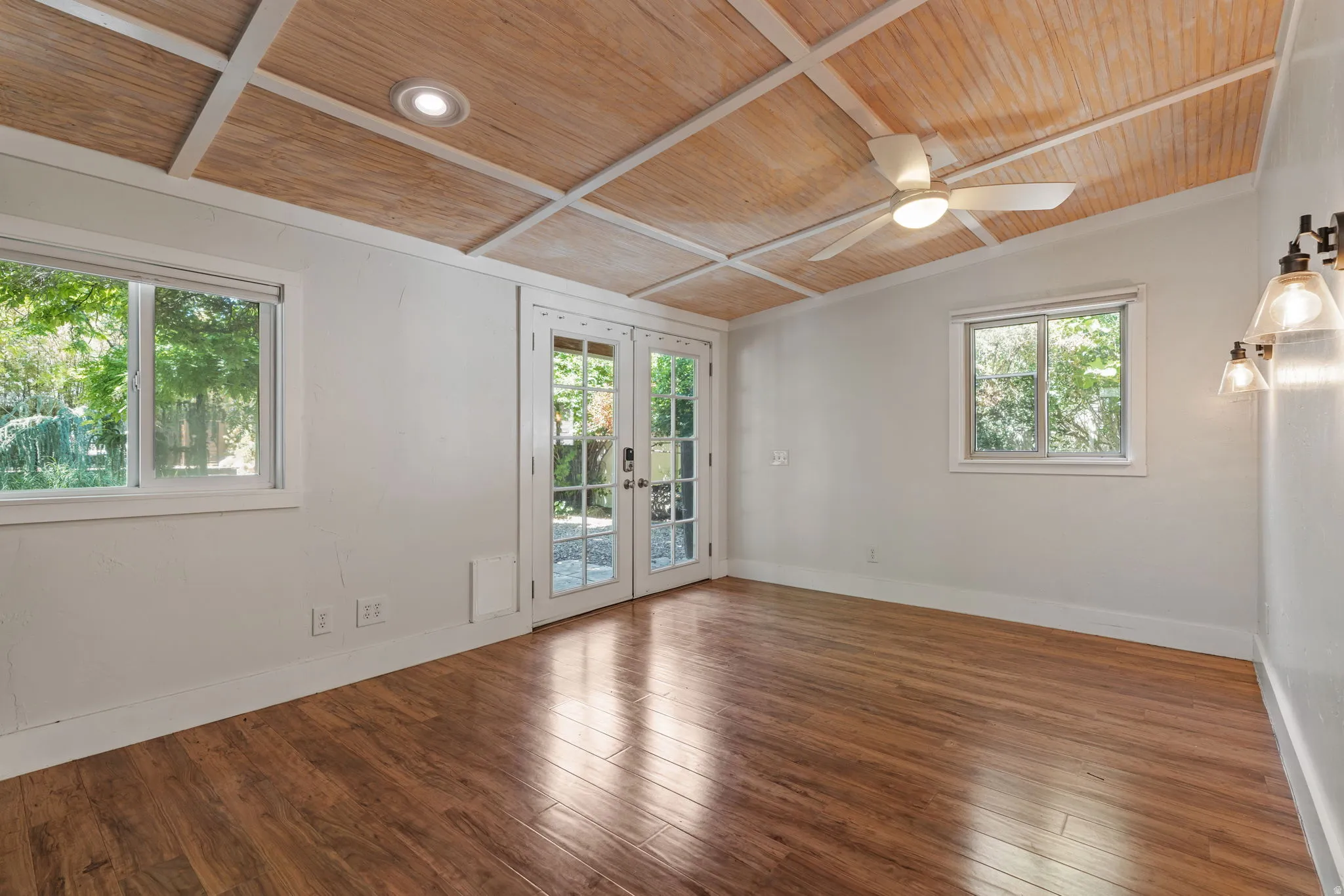 Vaulted wood-paneled ceiling with white beam accents, complemented by wood-finish flooring leading out to garden area through double French doors