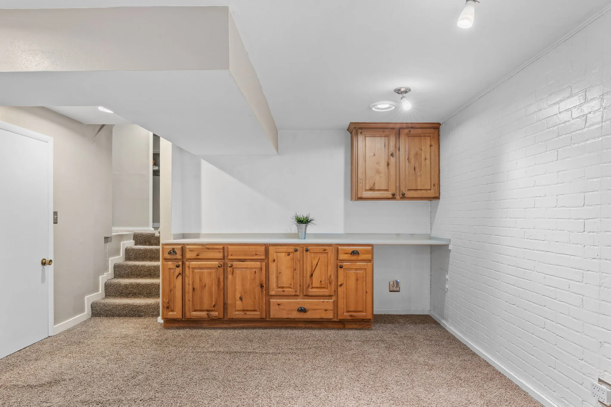 Lower level space featuring built-in wood cabinetry, a light-colored countertop, and a white painted brick accent wall