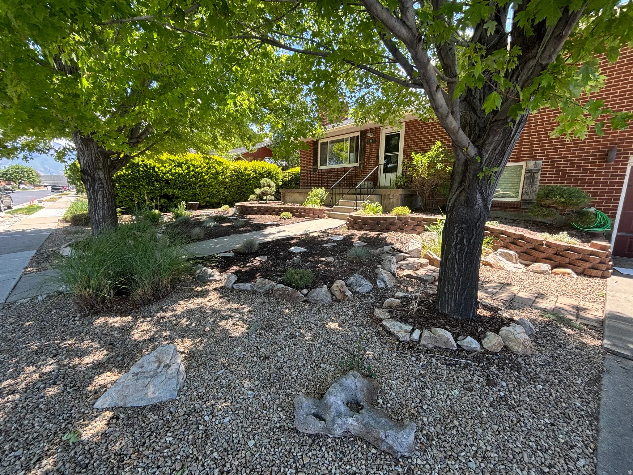 Brick exterior with white trim, featuring a concrete walkway and mature shade trees
