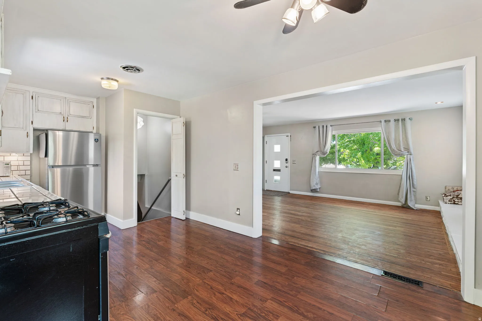 Open-concept room featuring wood-finish flooring, a kitchen area with white cabinetry and subway tile backsplash, and a living area with a large window