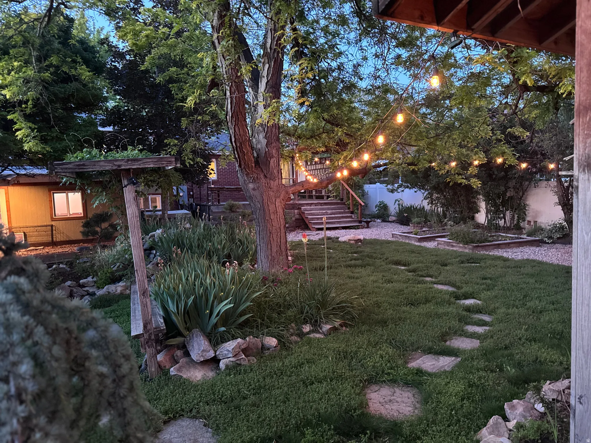 Landscaped backyard featuring alternative lawn pathway with stone pavers, mature trees, and raised garden beds