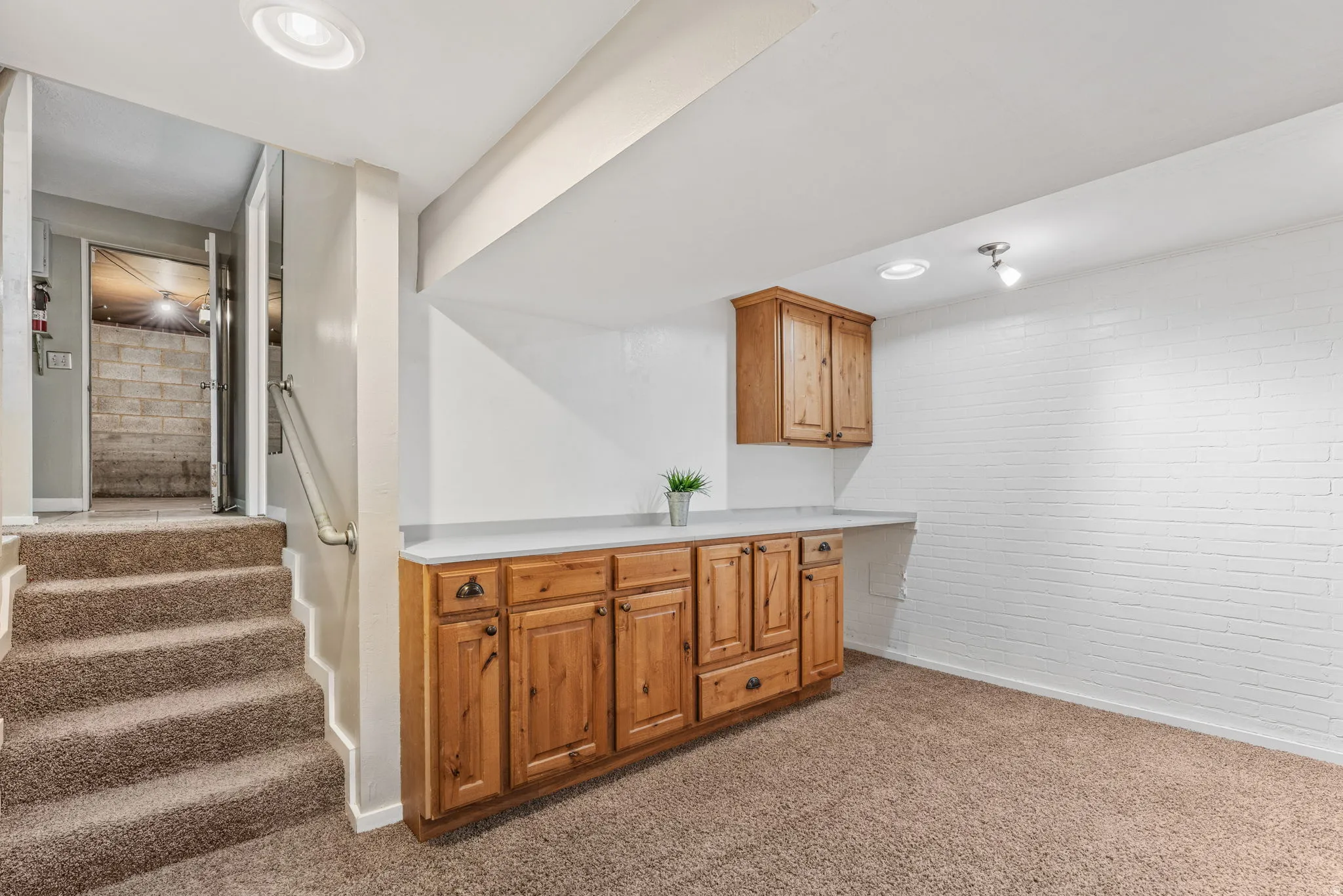 Built-in wood cabinetry with a light-toned countertop, recessed lighting, track lighting, and a white painted brick accent wall