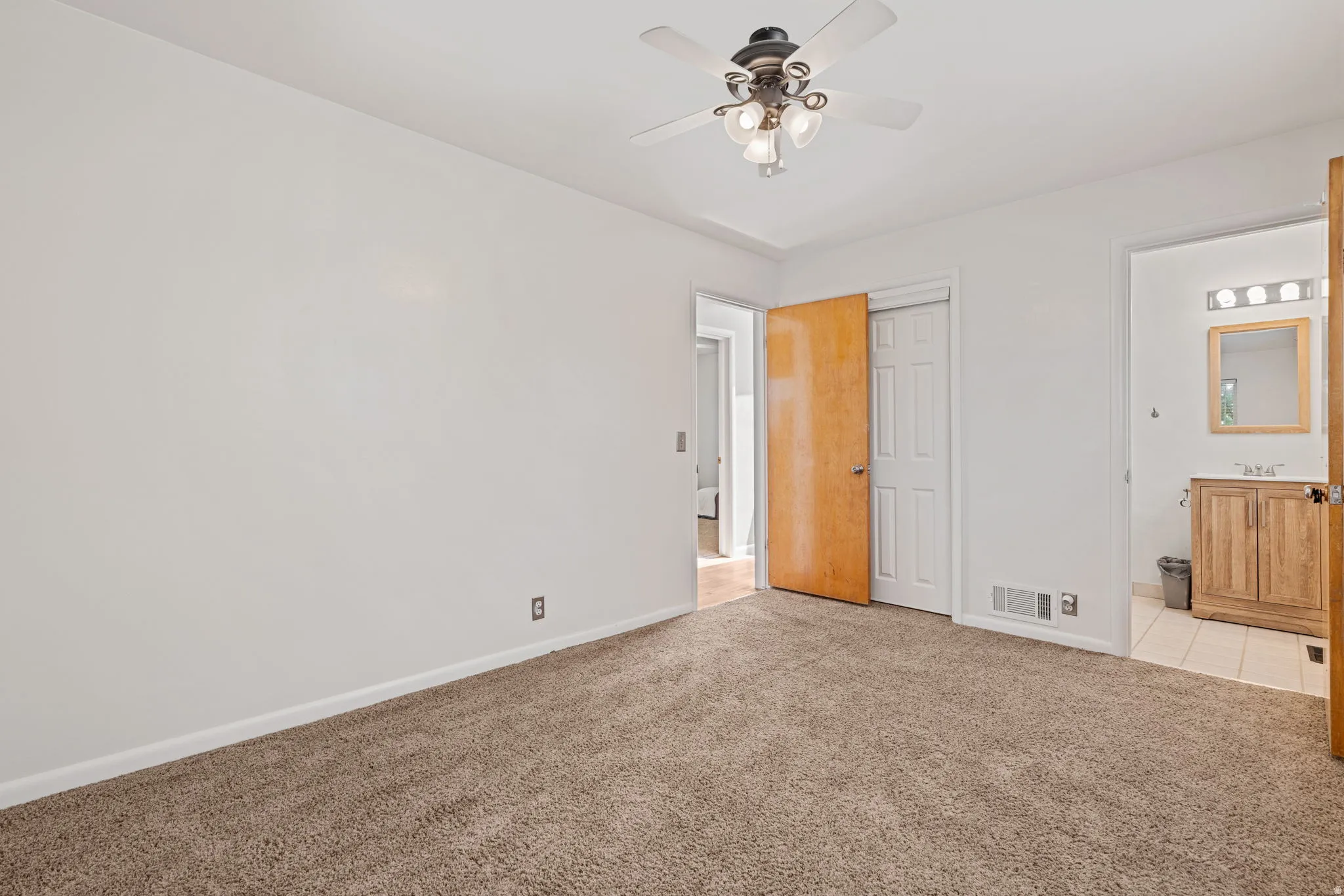 Carpeted room featuring a ceiling fan with integrated lighting, white walls, and wood-finish doors