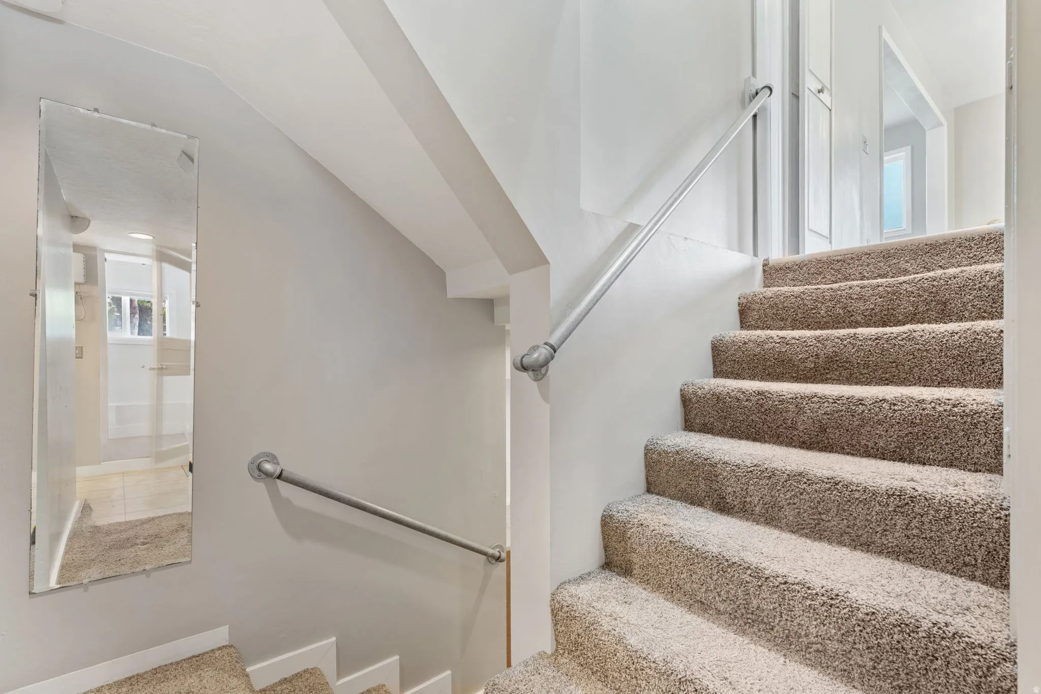Carpeted staircase with metal handrails from kitchen to first basement level (ground level)