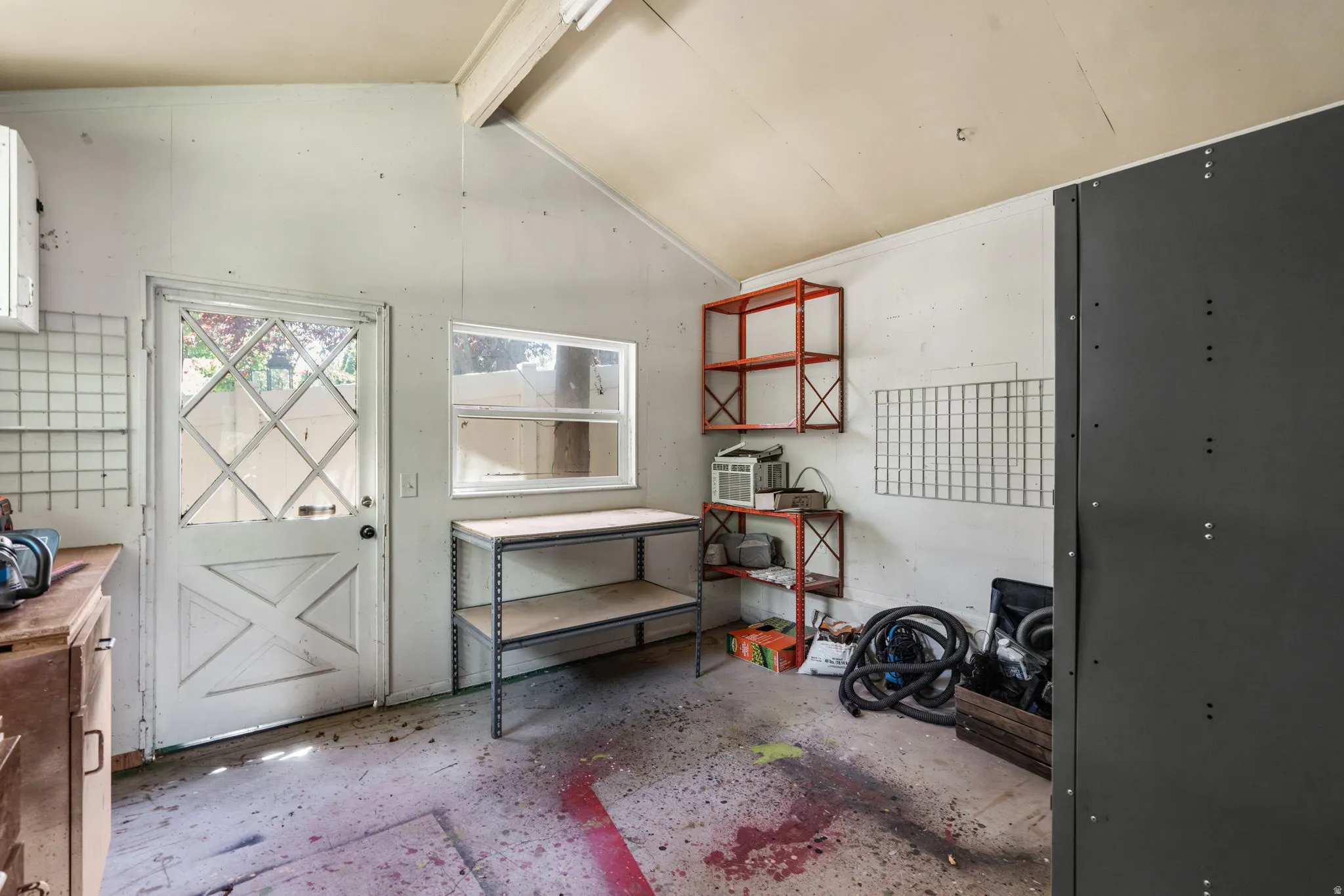 Interior utility space featuring a partial vaulted ceiling with beams, white walls, and a diamond-paneled glass door