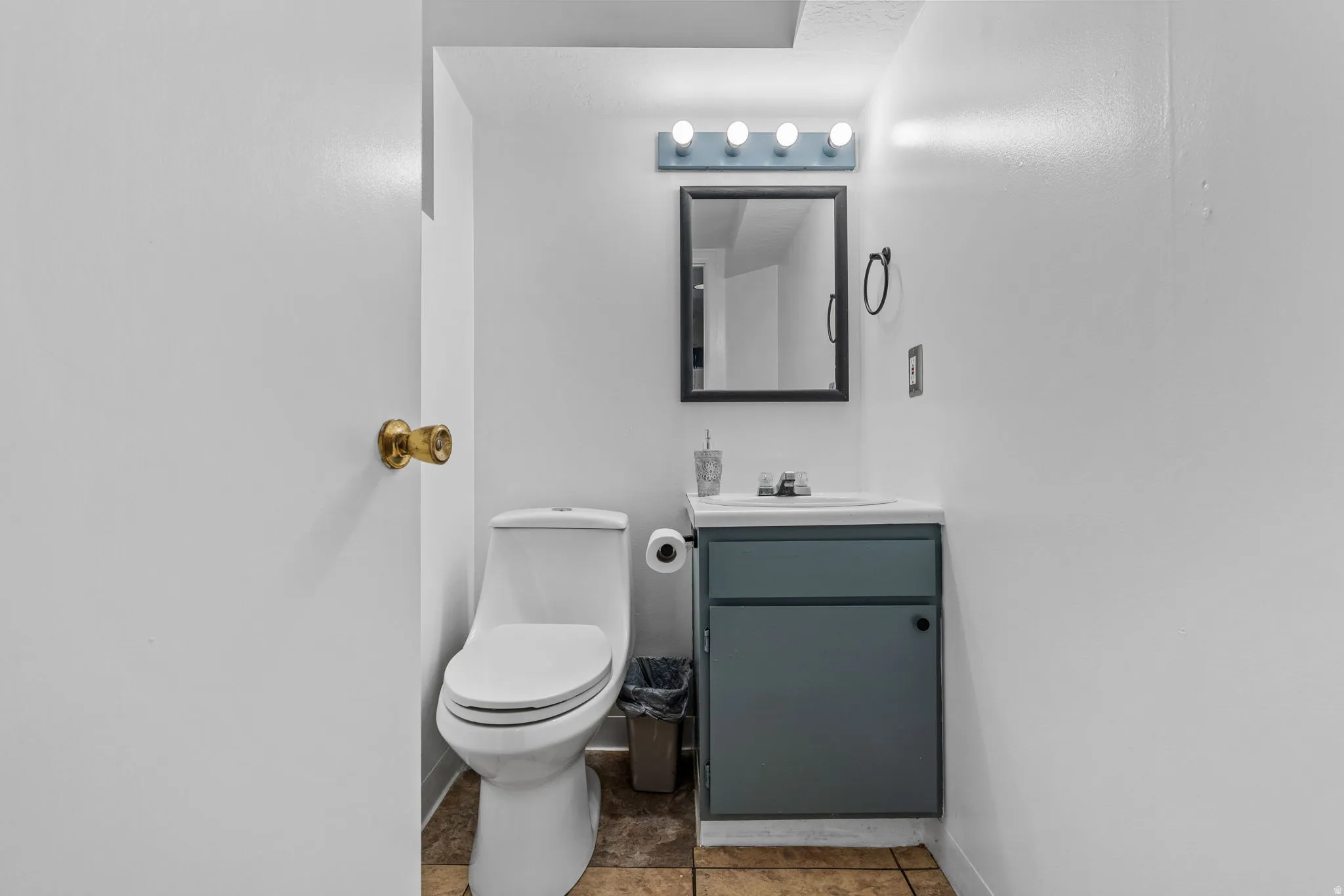 Compact bathroom featuring a white toilet, single-sink vanity with a blue-grey cabinet, and a framed mirror