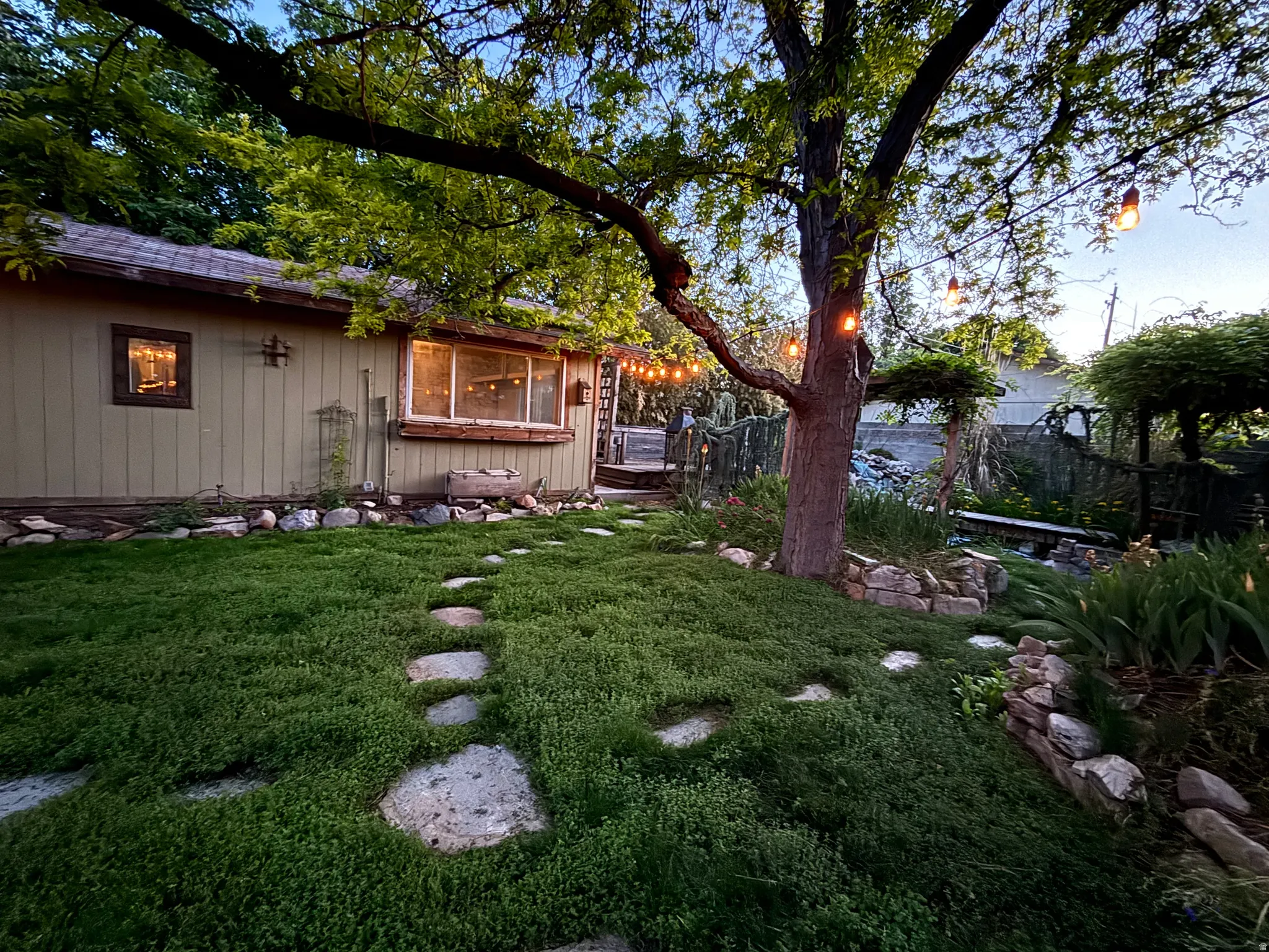 Landscaped backyard featuring a stone stepping path, established trees, and string lighting
