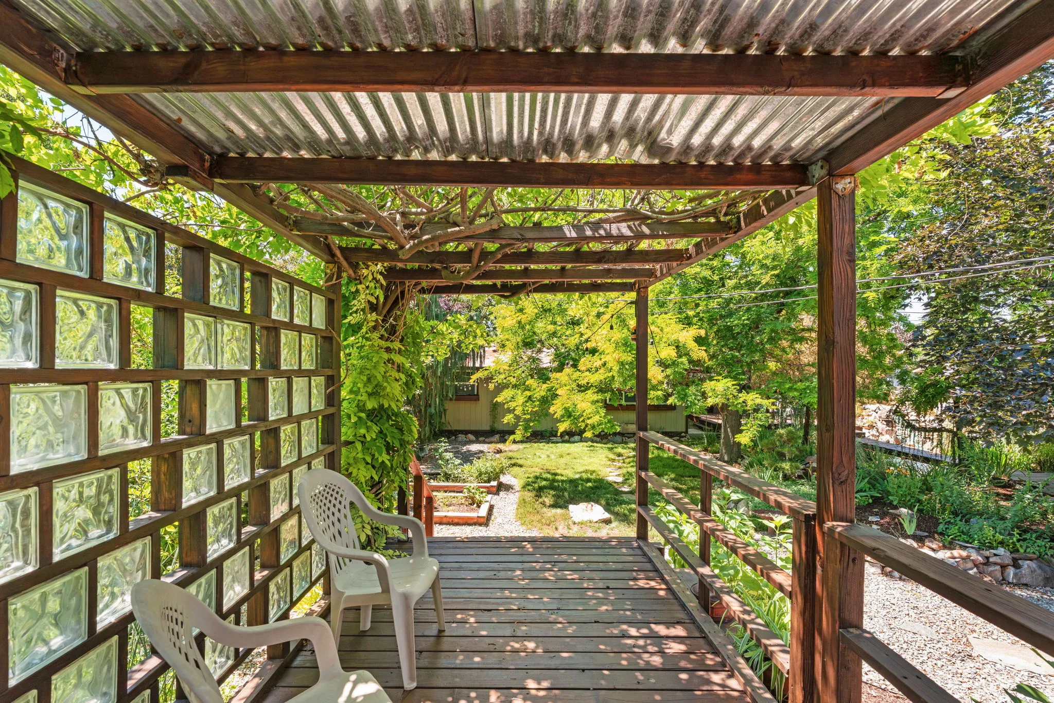 Outdoor deck featuring a corrugated metal roof and wood-finish railing and established wisteria growing overhead