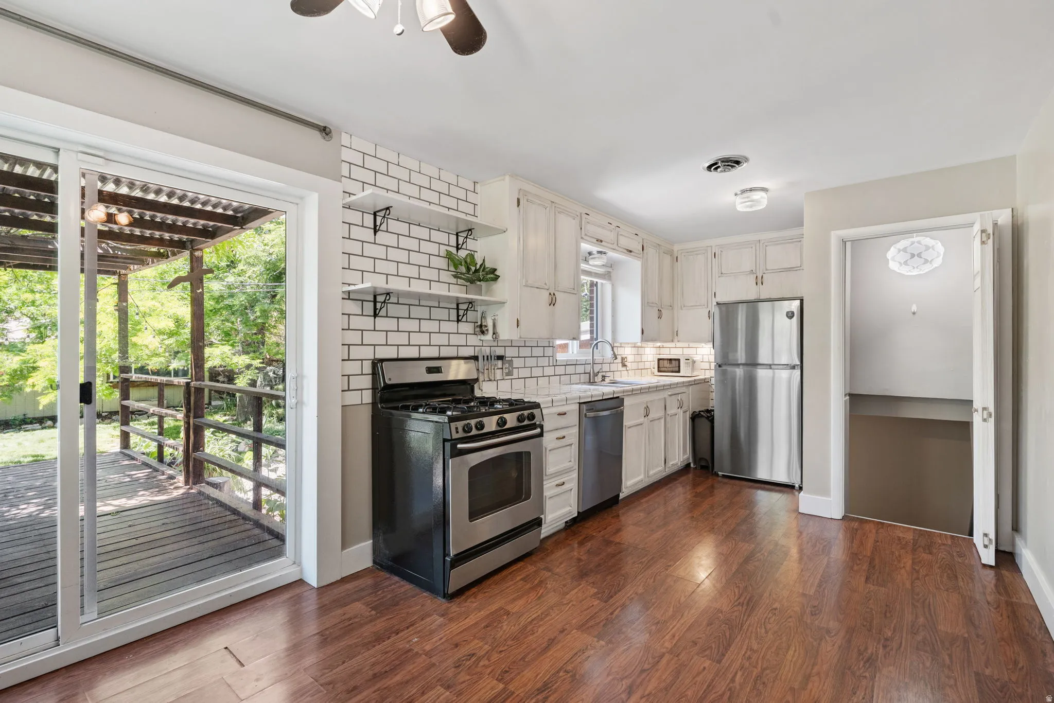 Kitchen featuring wood-finish flooring, white cabinetry, a subway tile backsplash, and stainless steel appliances