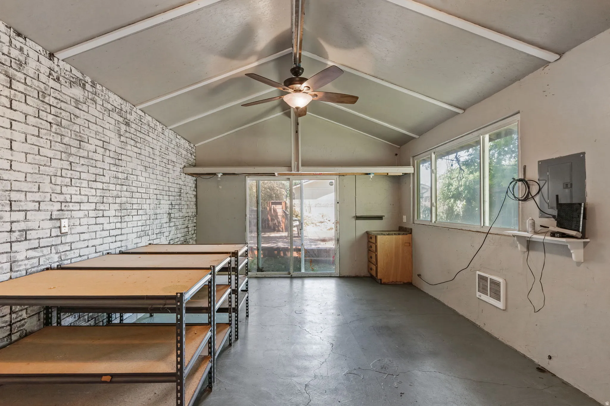 Spacious room featuring a vaulted ceiling with beams, painted brick accent wall, and concrete flooring and heater