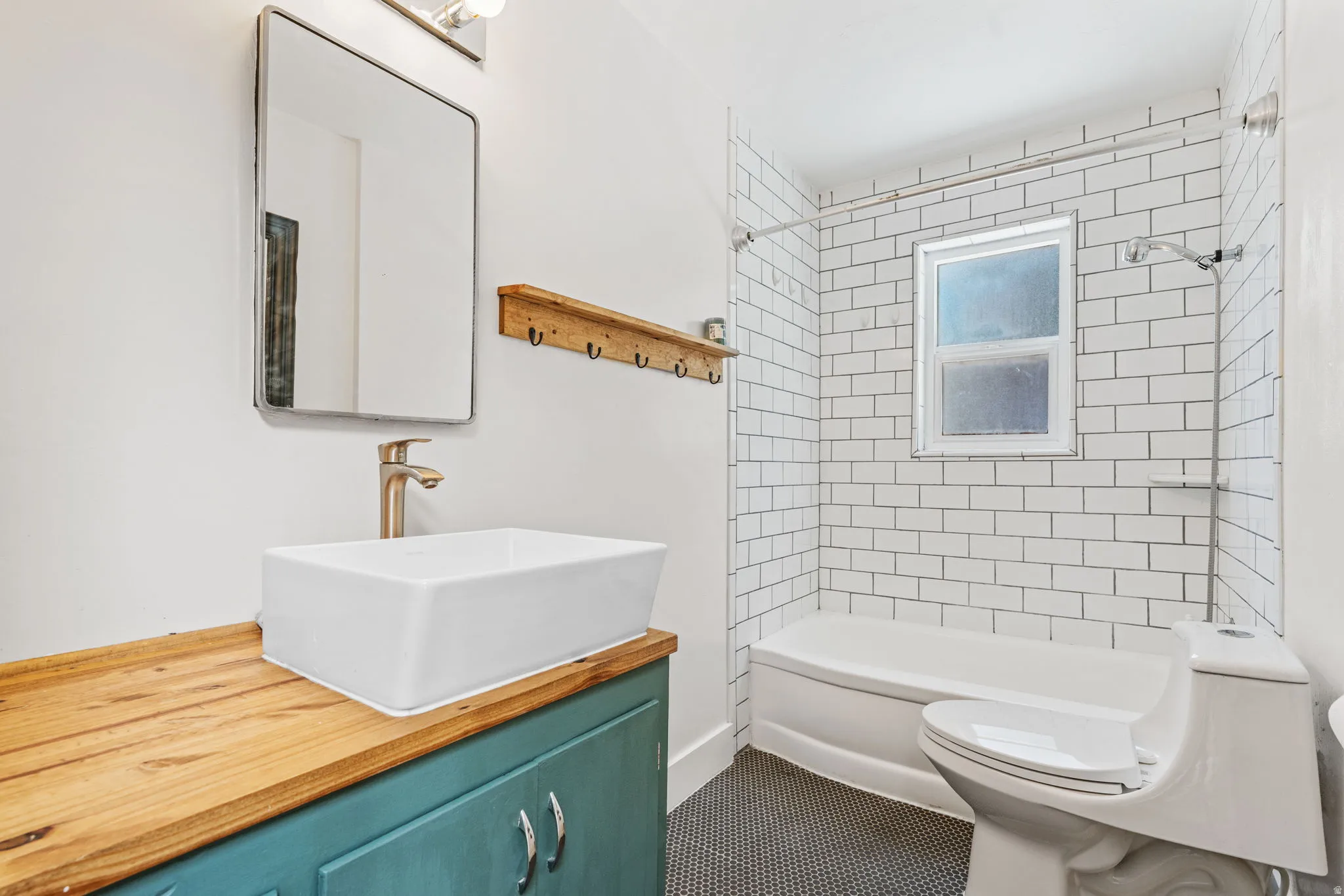 Bathroom featuring a vessel sink with a brushed brass faucet, a wood-finish vanity countertop, a subway tile shower surround with a window, a white bathtub, and hexagonal floor tile